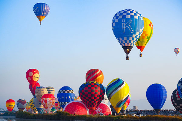 Cluster of colorful hot air balloons on the ground preparing for flight under a clear blue sky.