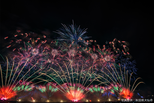 Multicolored fireworks illuminating a dark night sky above a calm harbor.