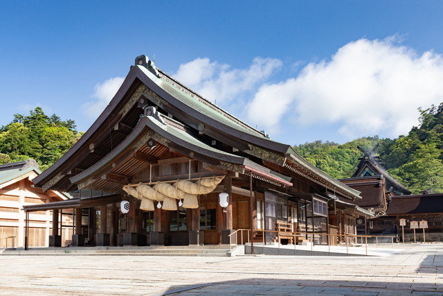 Shinto shrine building with wooden architecture, large straw rope (shimenawa) and paper lanterns on a sunny day