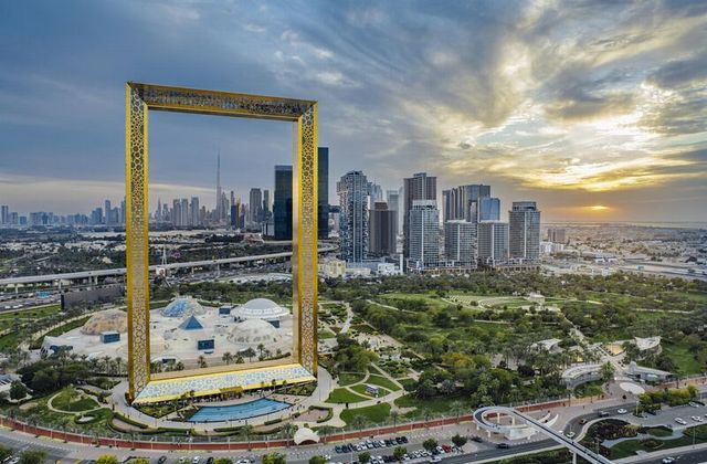 Golden ornate frame in a park framing Dubai's high-rise skyline at sunset due to the golden hour light.
