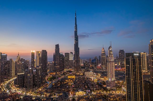 City skyline at dusk with the Burj Khalifa towering above illuminated skyscrapers in downtown Dubai.