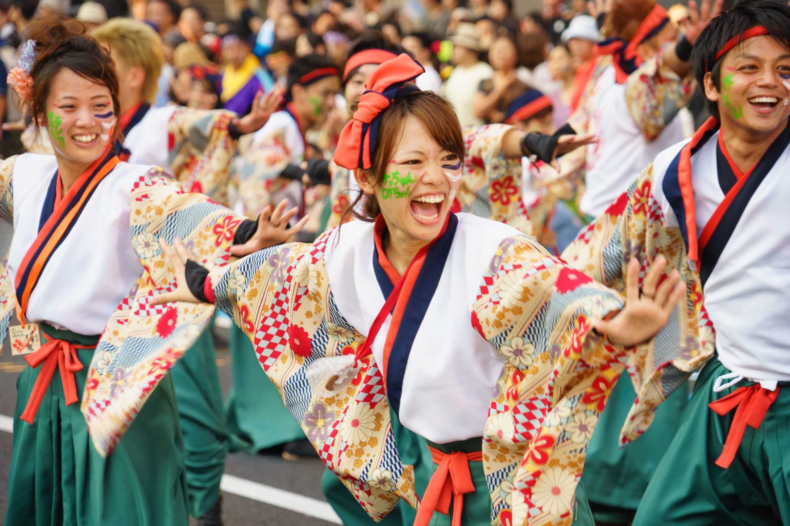 Group of dancers in bright floral kimonos performing at a festival, smiling and moving energetically.