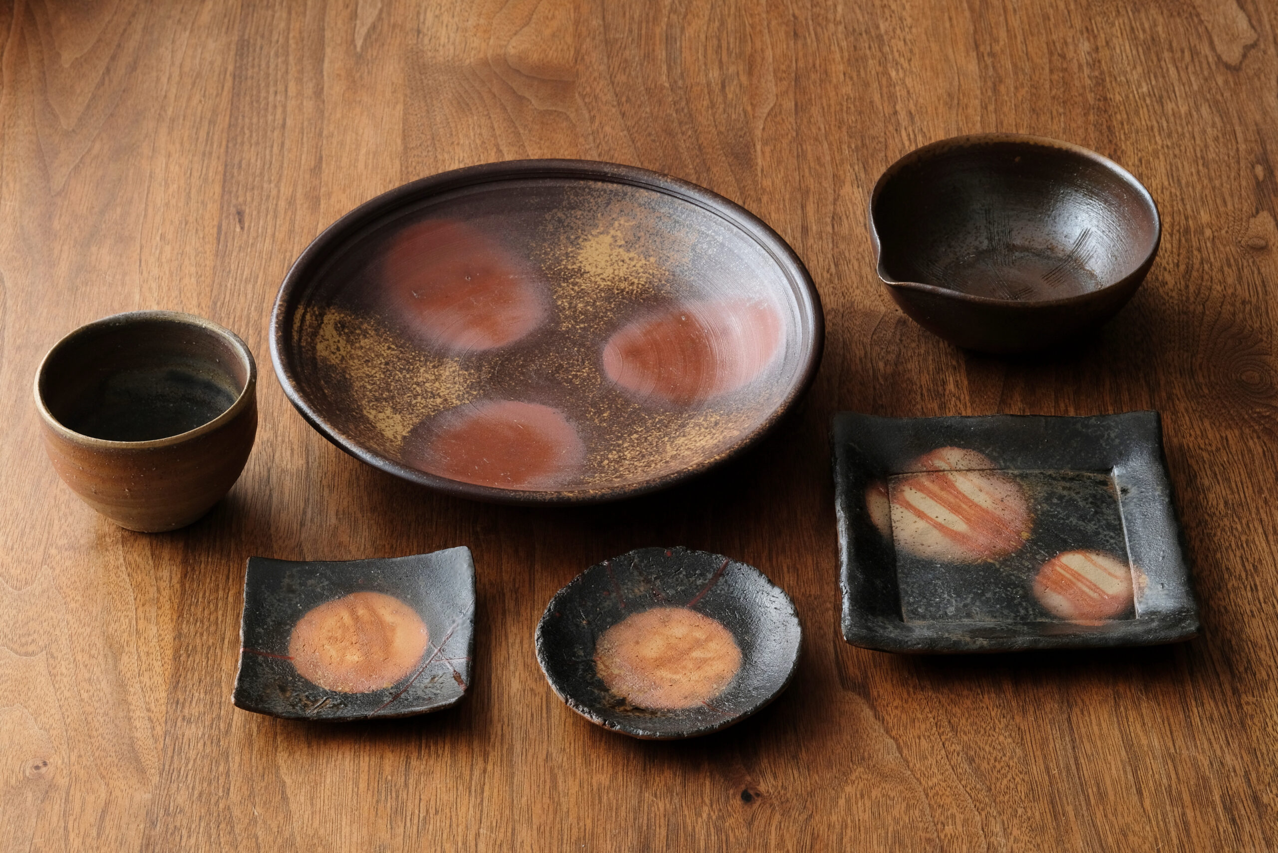 Set of handmade ceramic bowls and plates arranged on a wooden table surface