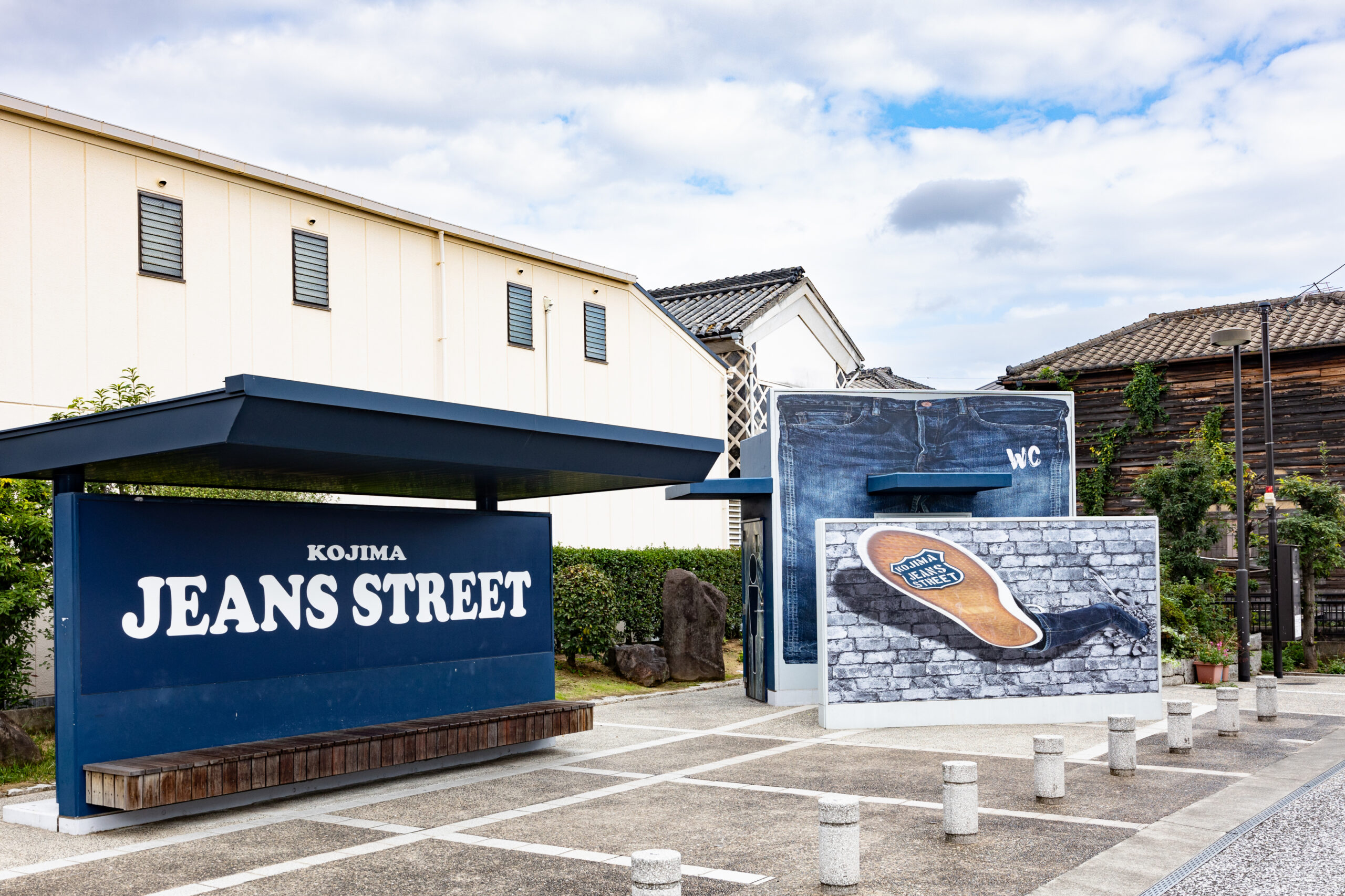 Blue sign reading KOJIMA JEANS STREET in front of a beige building and denim-themed display.