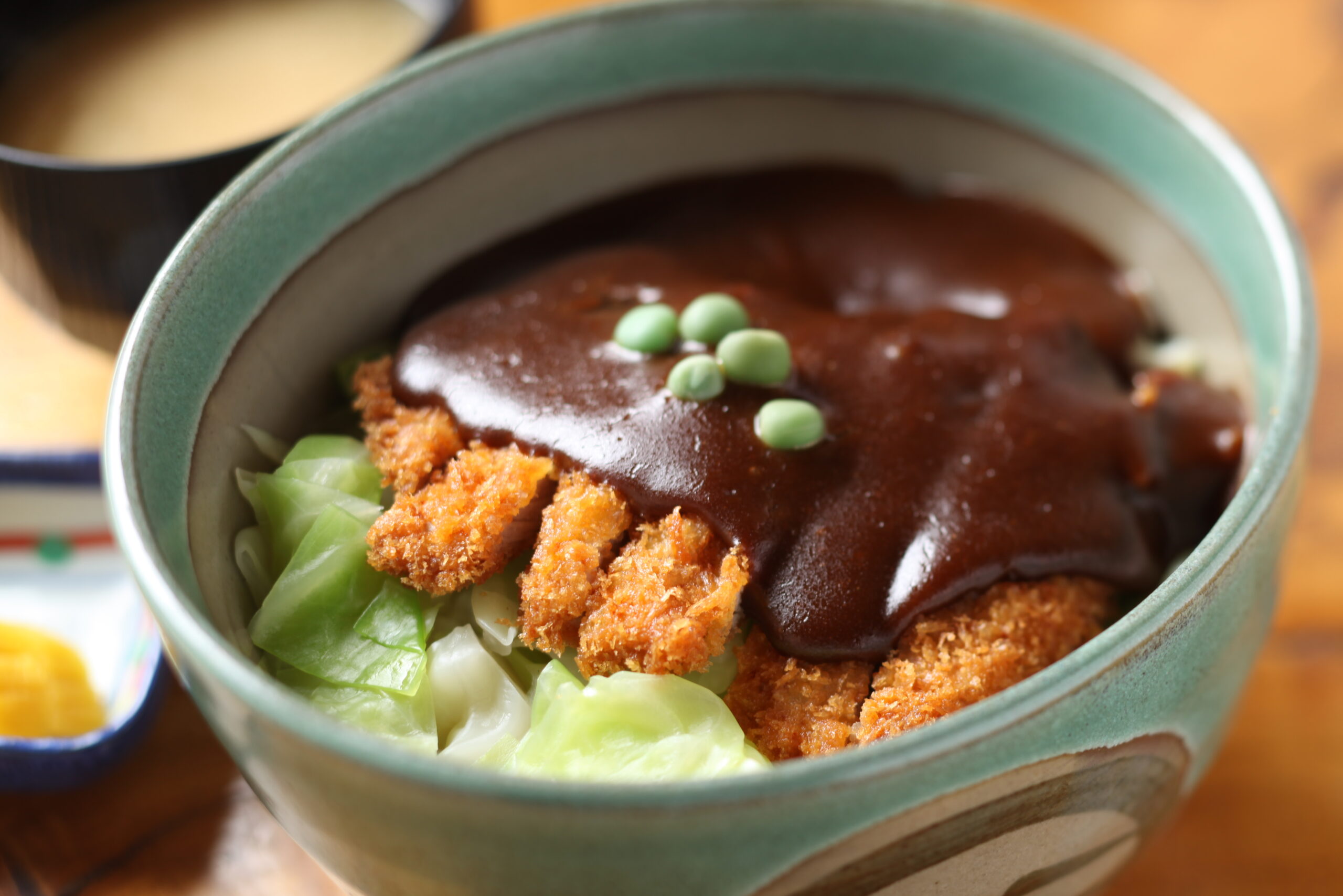 Green ceramic bowl with crispy fried chicken pieces, glossy brown sauce, and shredded lettuce.