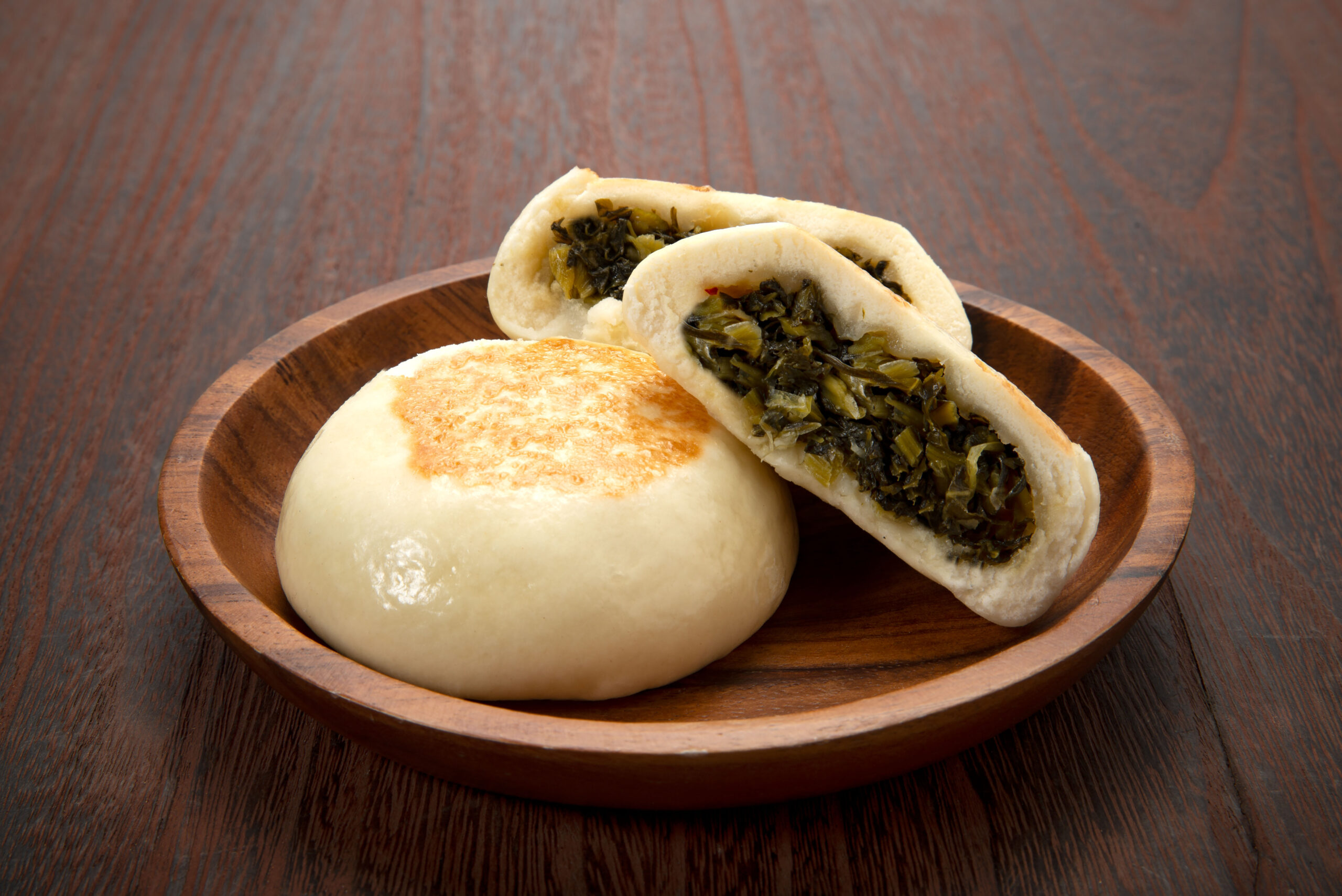 Steamed buns with a leafy green filling on a wooden plate