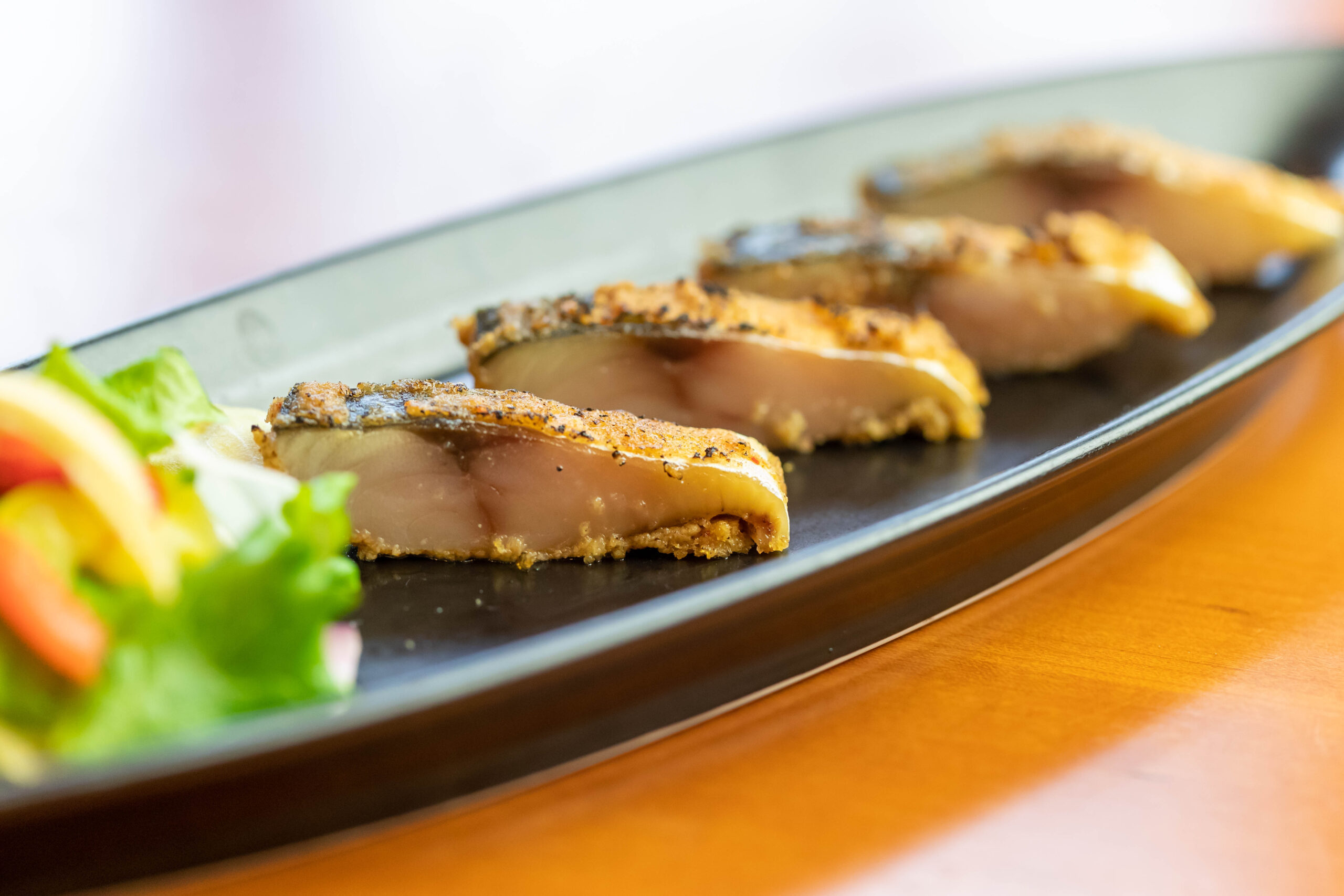 Slices of crusted roasted meat arranged on a dark plate with a side of greens at the edge.
