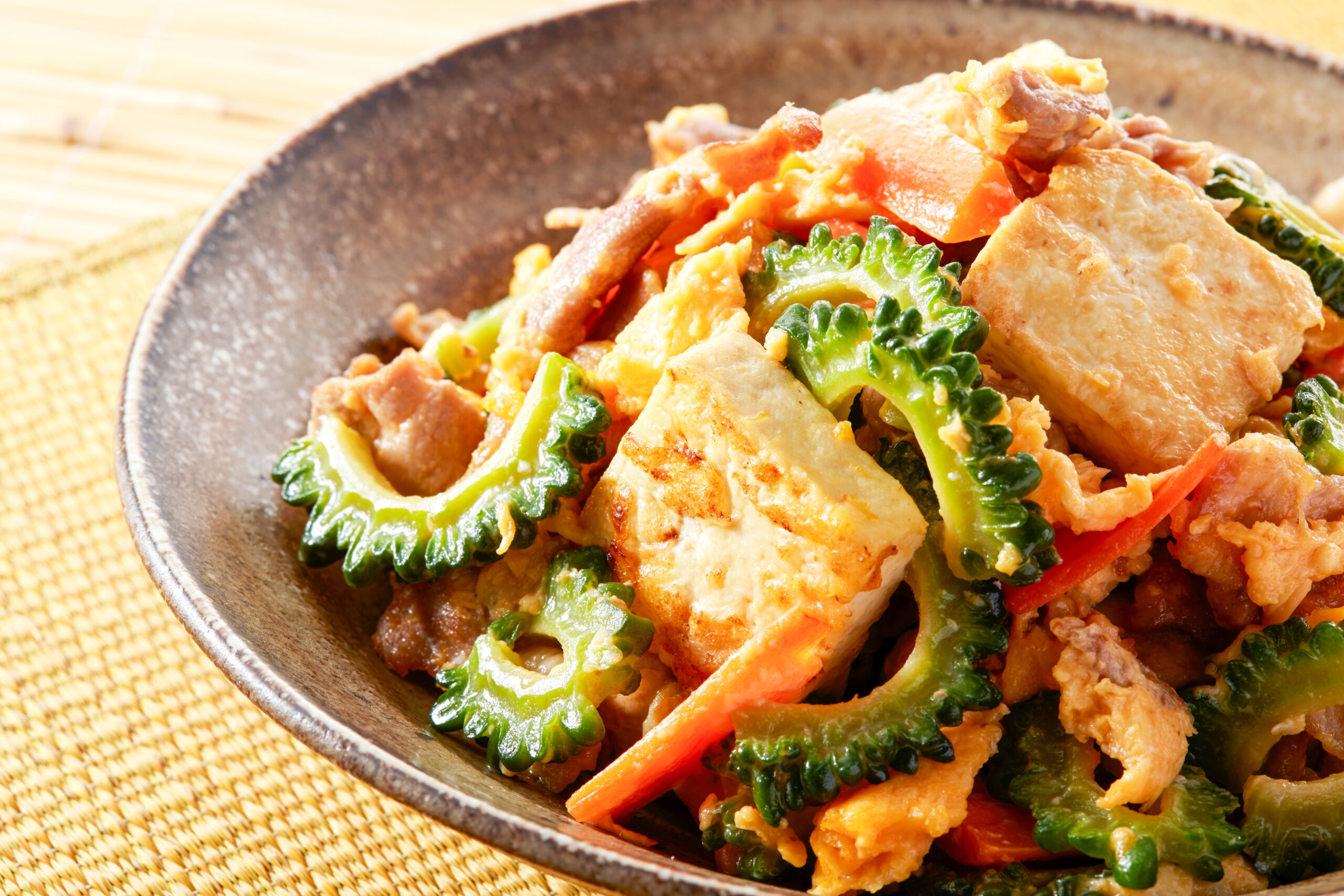 Stir-fry with chicken, eggs, carrots and bitter melon in a dark ceramic bowl on a woven mat