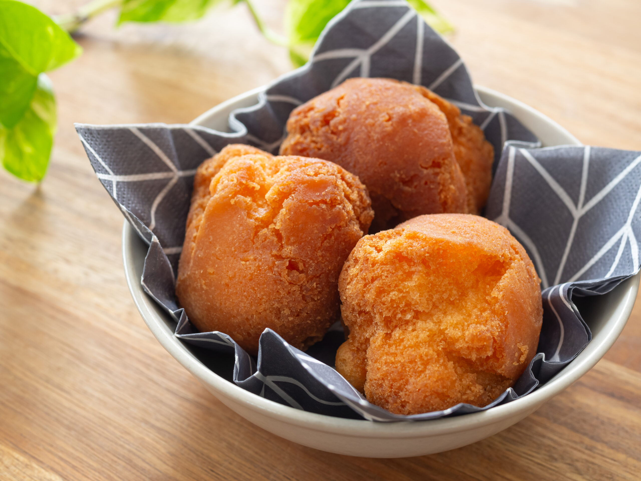 Bowl of orange fried dough balls lined with a geometric napkin on a wooden table