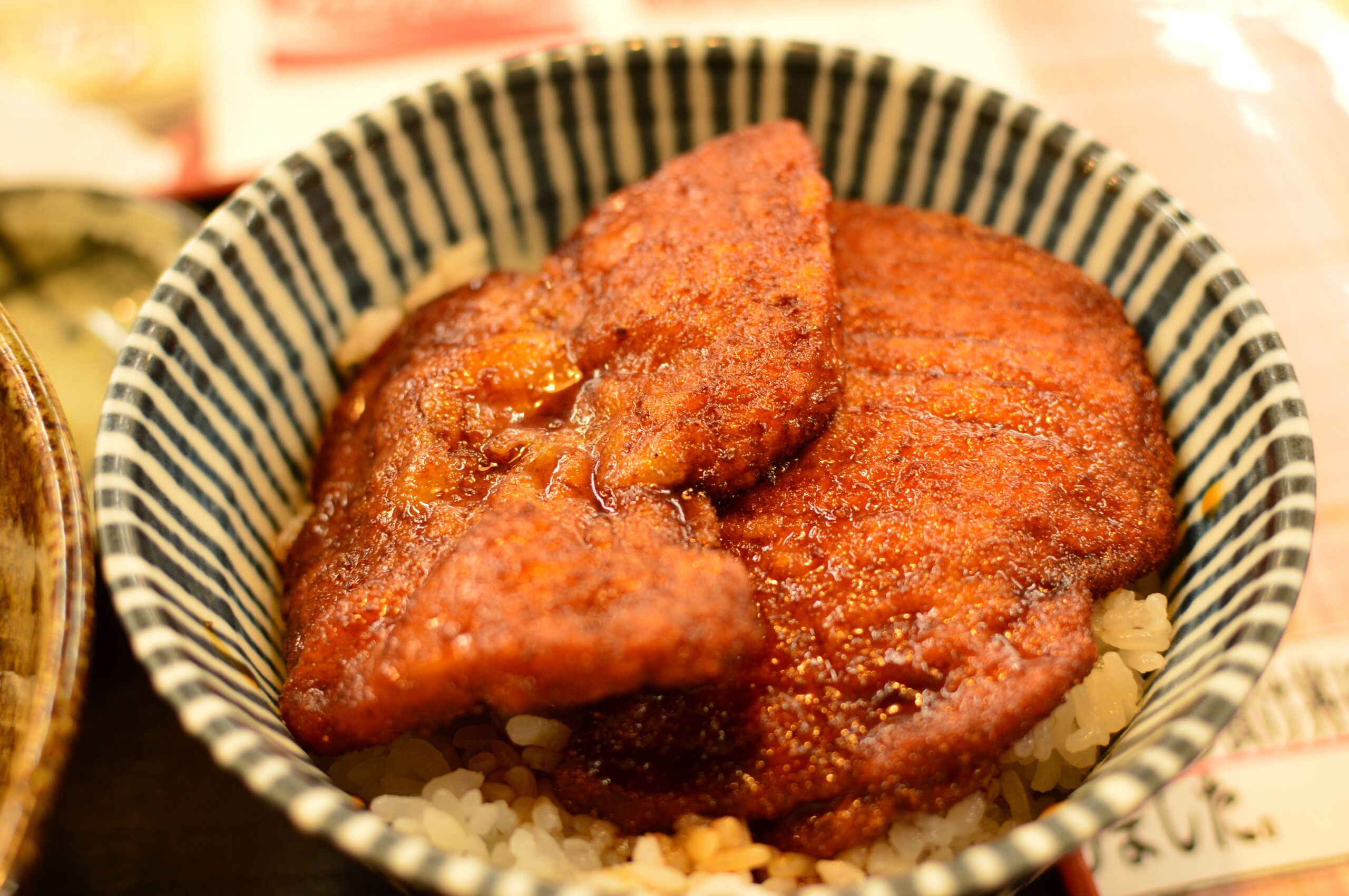 Glazed grilled meat on a bed of white rice in a blue-and-white striped bowl (donburi).