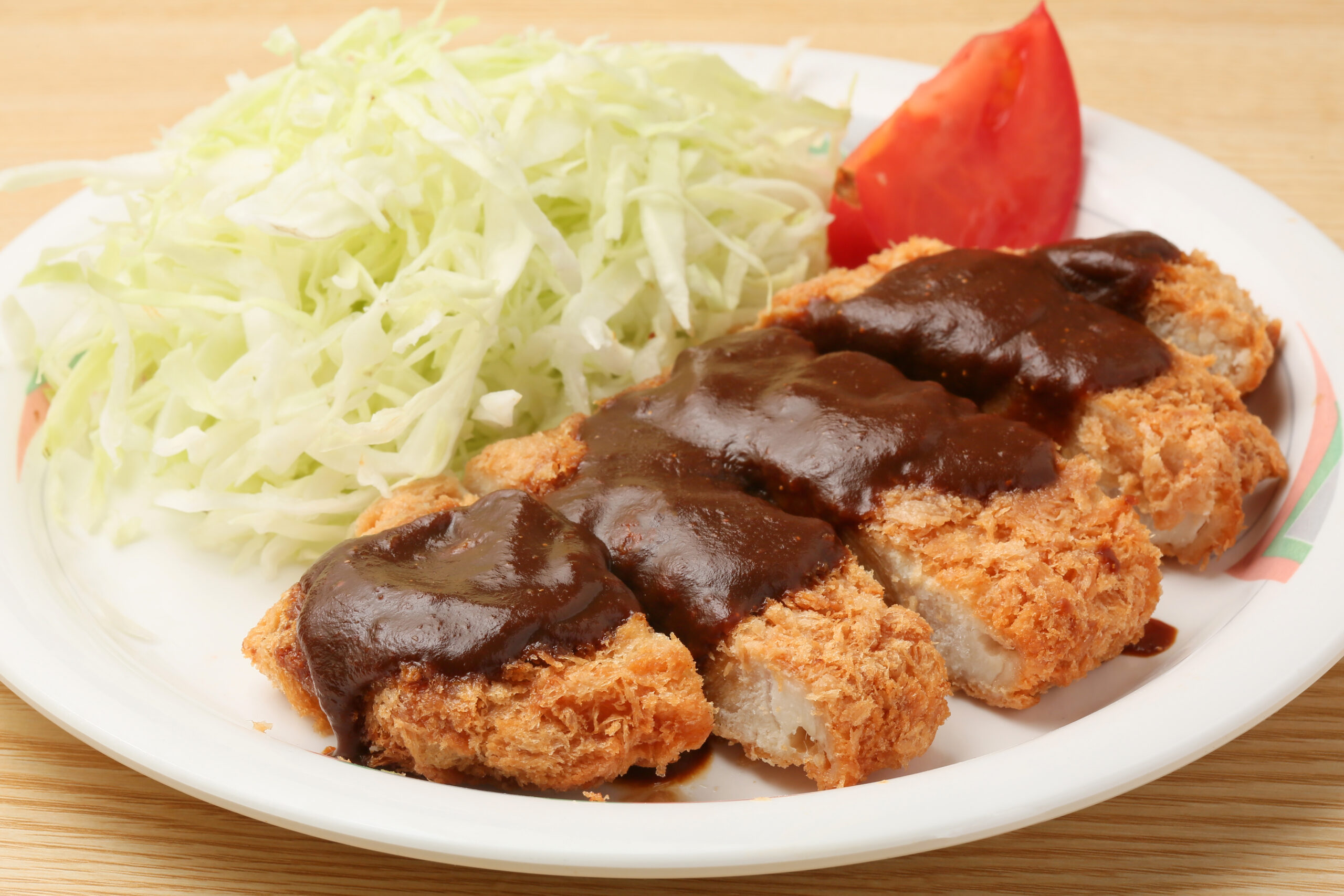 Crispy fried chicken cutlets topped with brown gravy, with shredded cabbage and a tomato wedge on a plate.