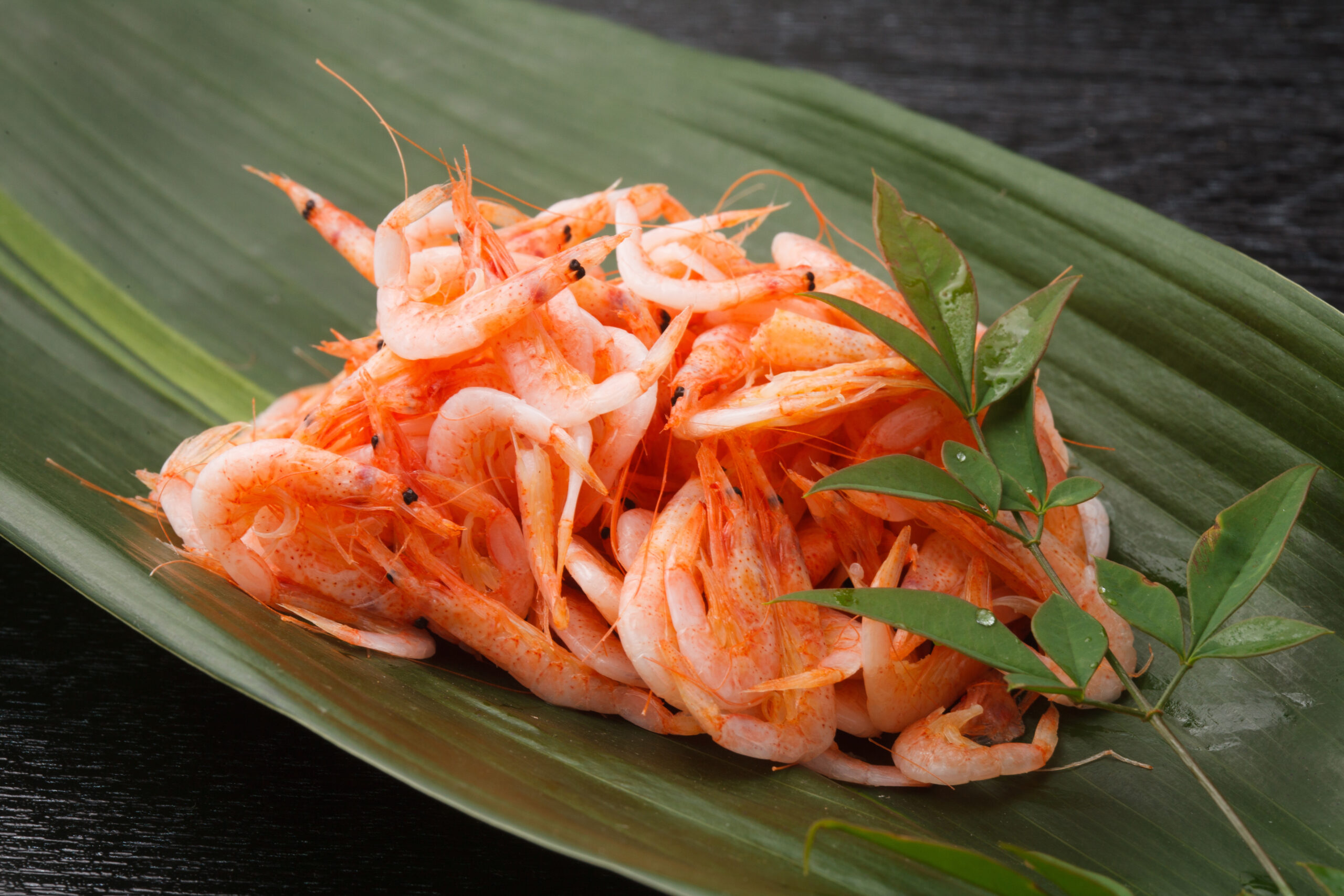 Pile of orange-pink shrimp on a large green banana leaf, ready to serve.