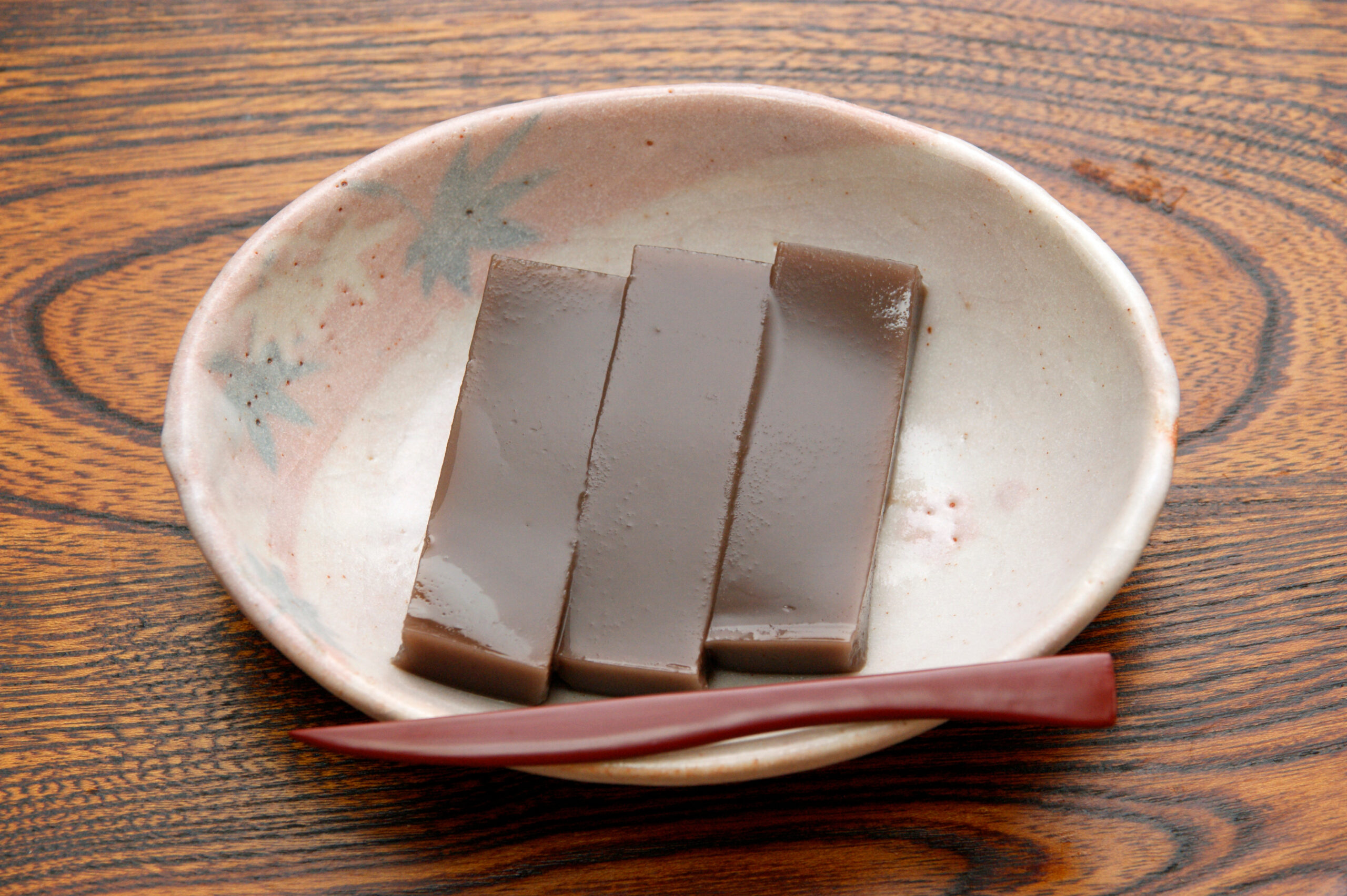 Several rectangular pieces of dark chocolate arranged on a light ceramic plate, with a red utensil resting along the edge on a wooden table.