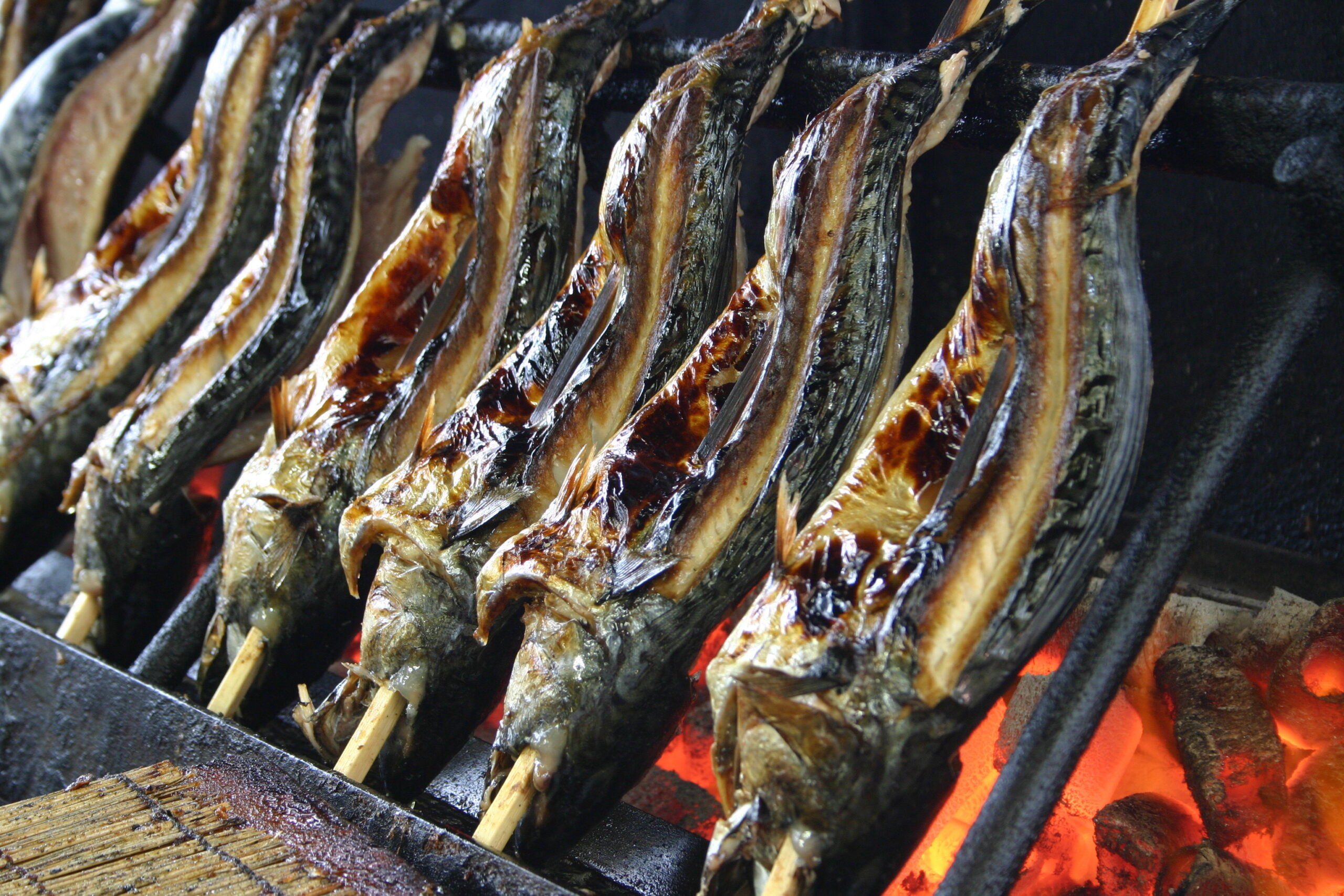 Fish on skewers grilling over hot charcoal with orange flames visible beneath.