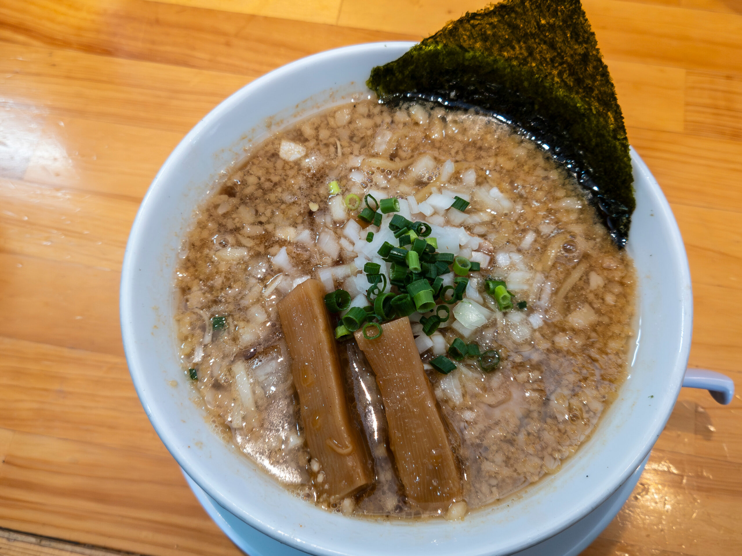 Bowl of ramen with a large sheet of seaweed, chopped onions, and green onions in broth (top-right focus).