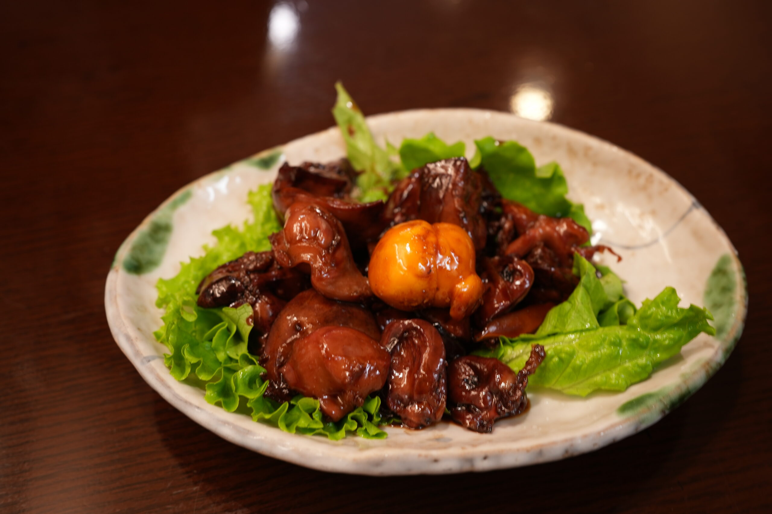 Plate of braised beef in a glossy brown sauce atop fresh lettuce on a decorative ceramic plate.