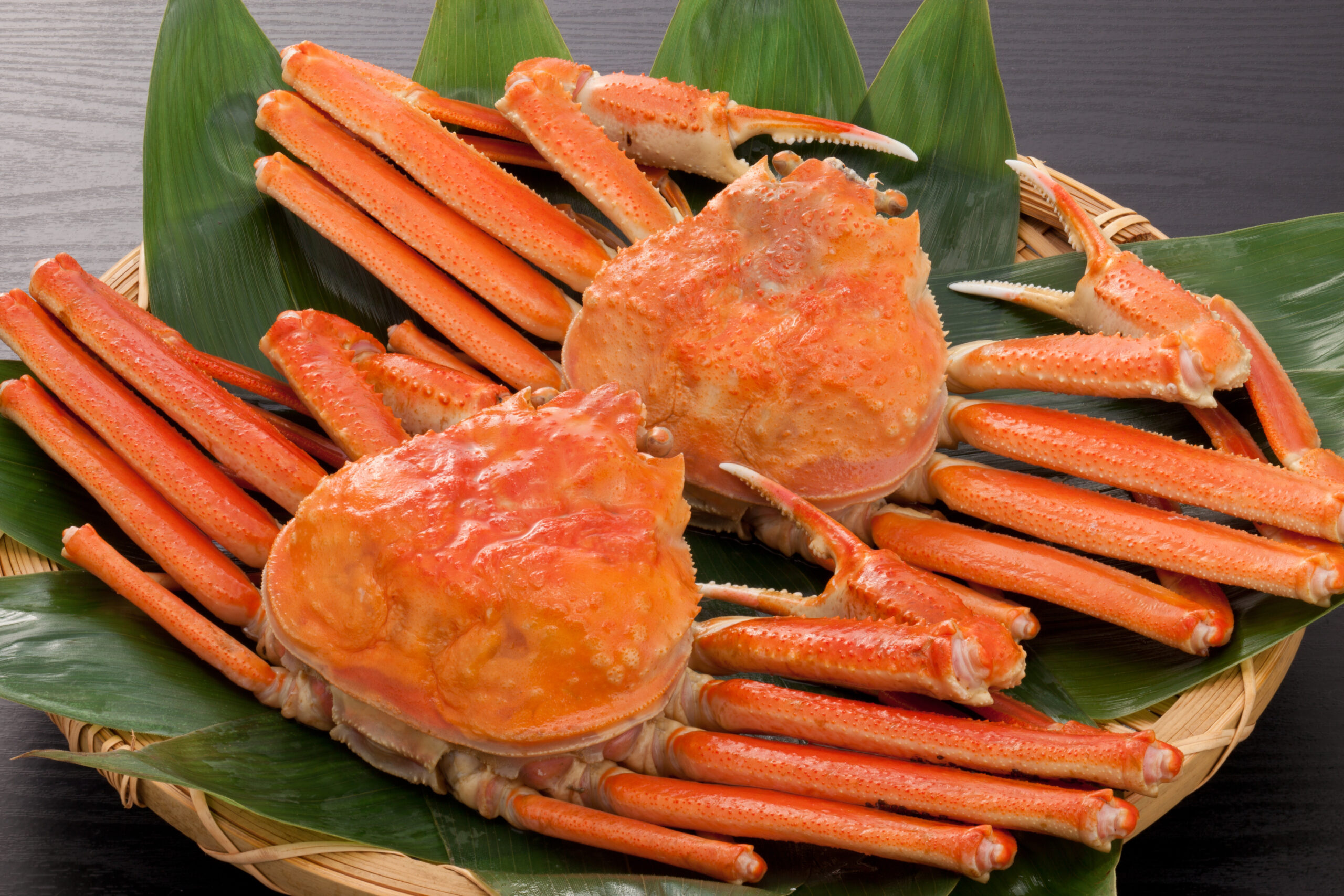 Crab legs arranged on a woven basket with large green leaves beneath them.