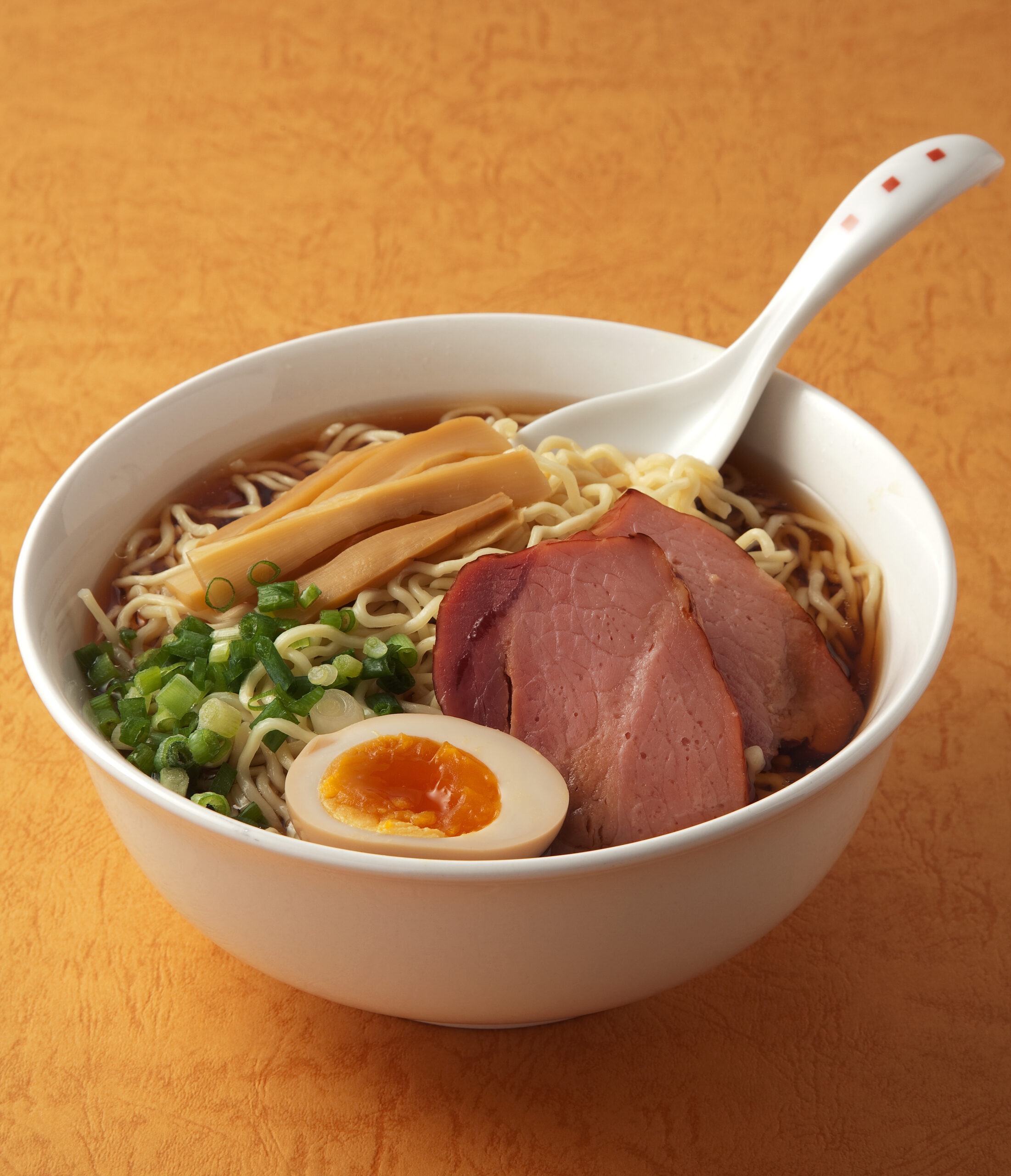 Bowl of ramen with sliced pork, a soft-boiled egg, green onions, and bamboo shoots in broth.