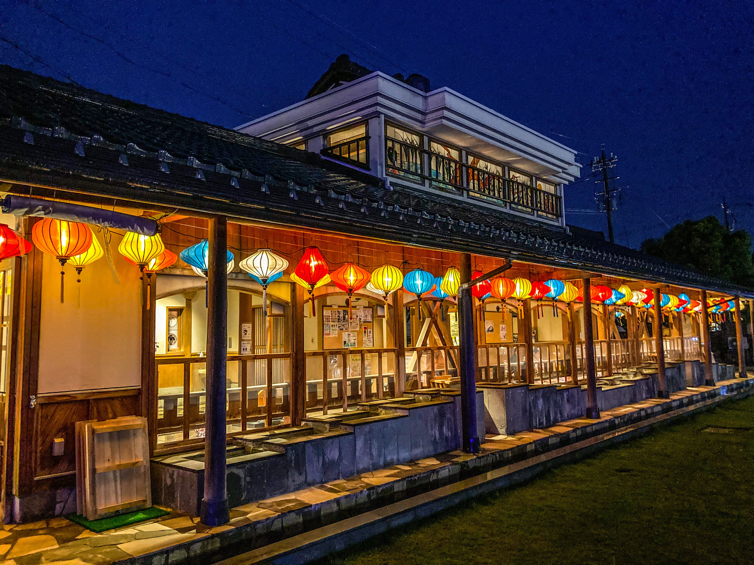 Night view of a traditional building with a row of colorful paper lanterns hanging along a covered walkway.