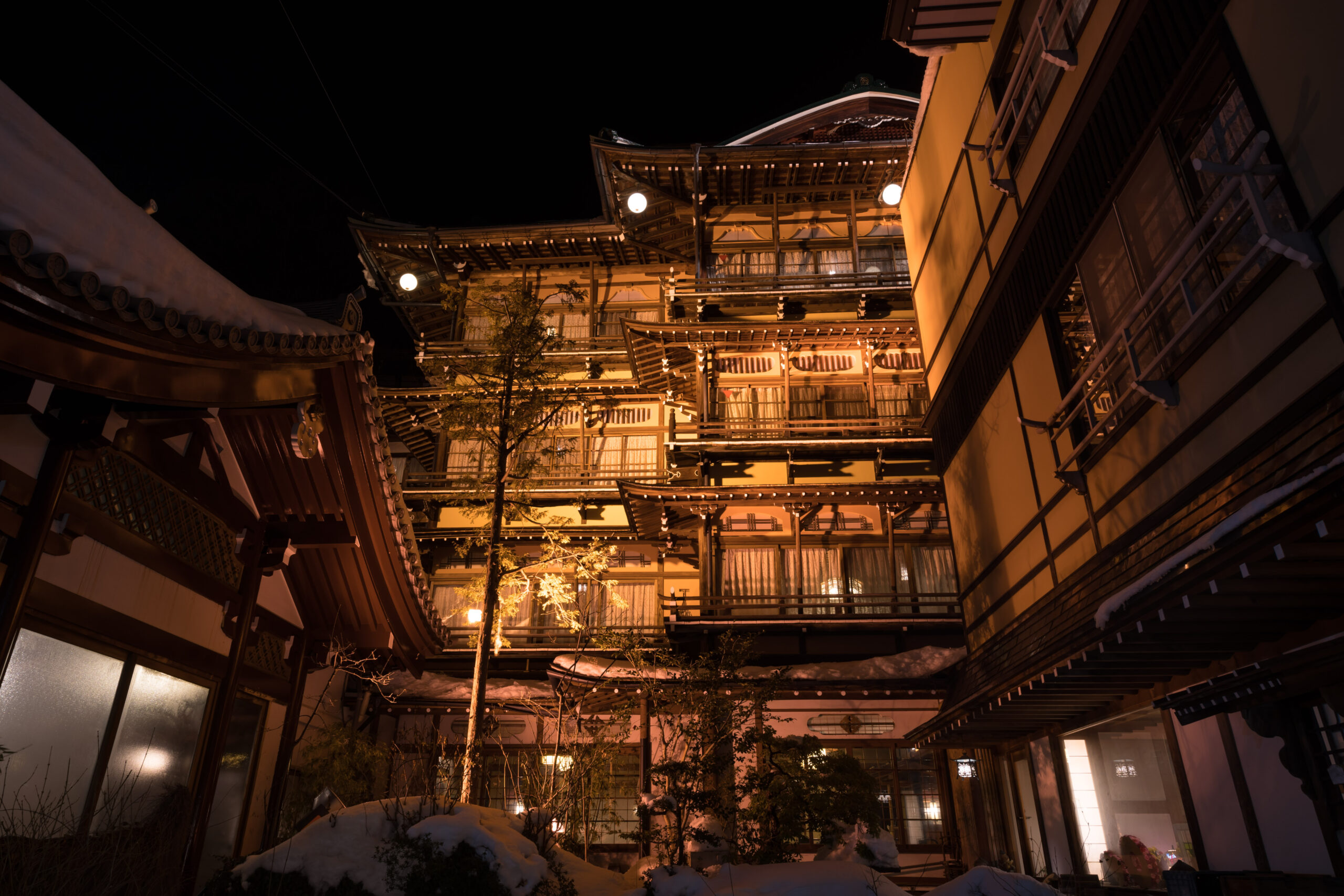 Traditional multi-story Japanese wooden inn (ryokan) at night with warm orange lights and snow on the ground
