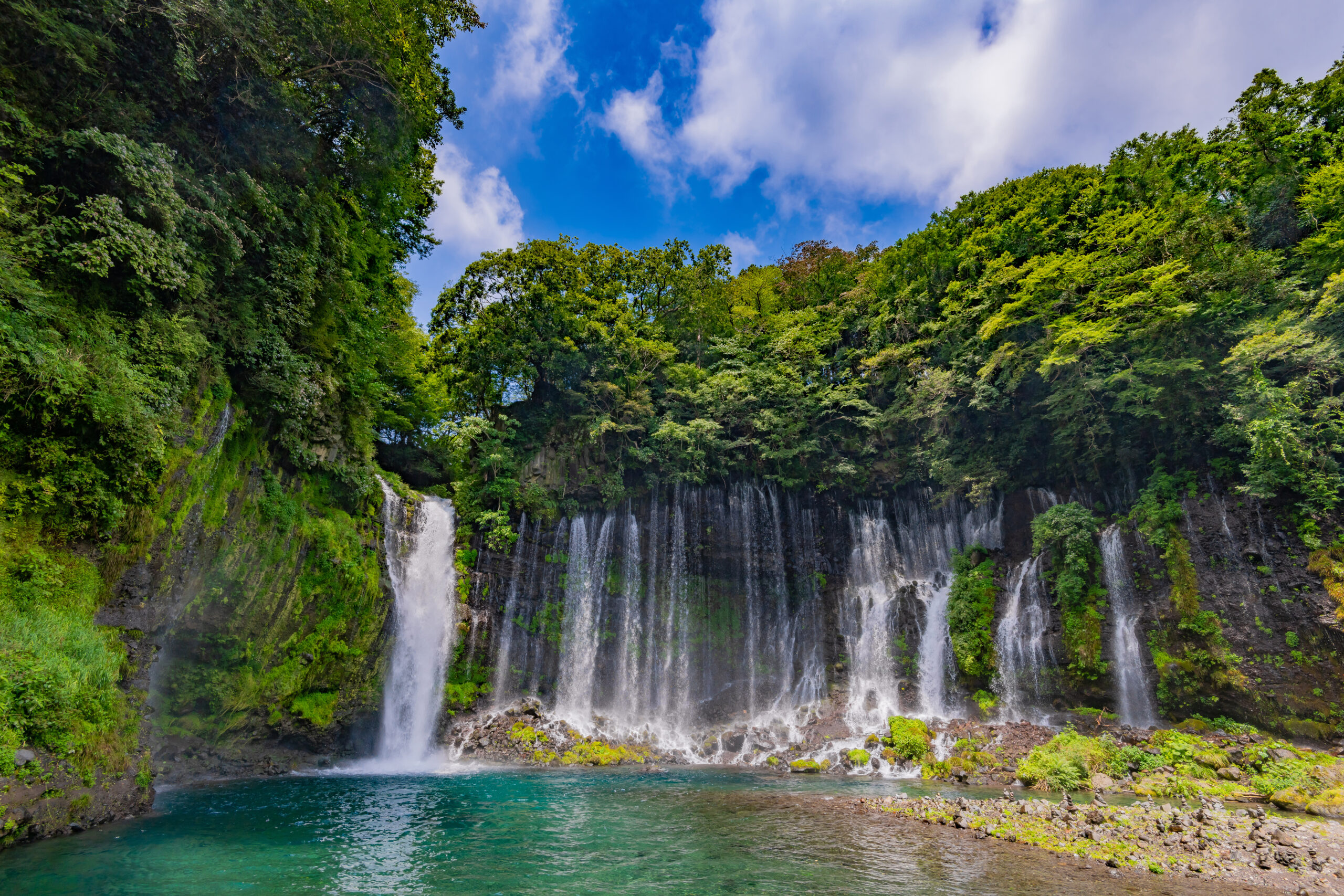 Waterfall cascading down a rocky cliff into a turquoise pool, surrounded by lush green forest. (informative)
