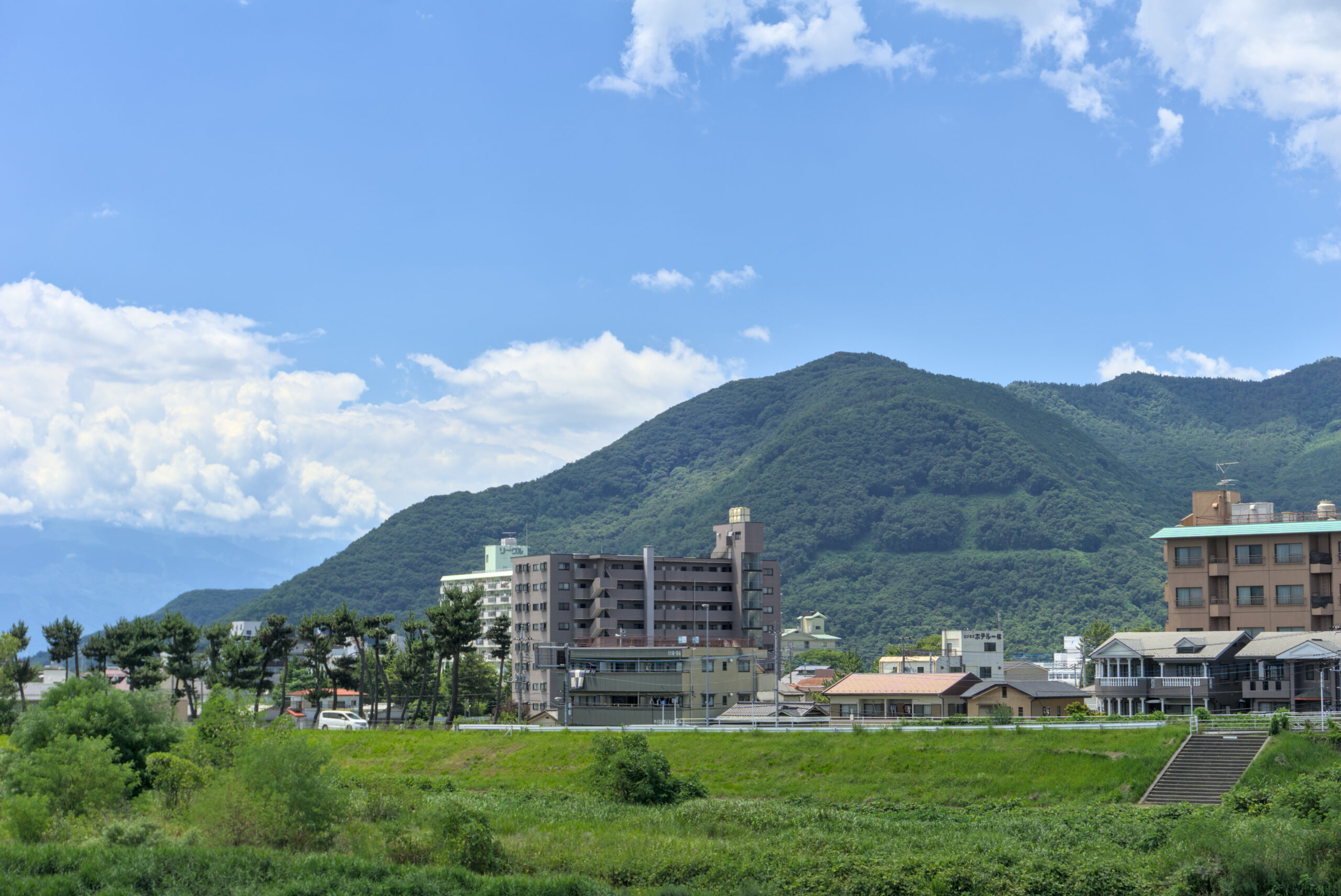 City buildings at the base of green hills with a blue sky and scattered clouds in the background