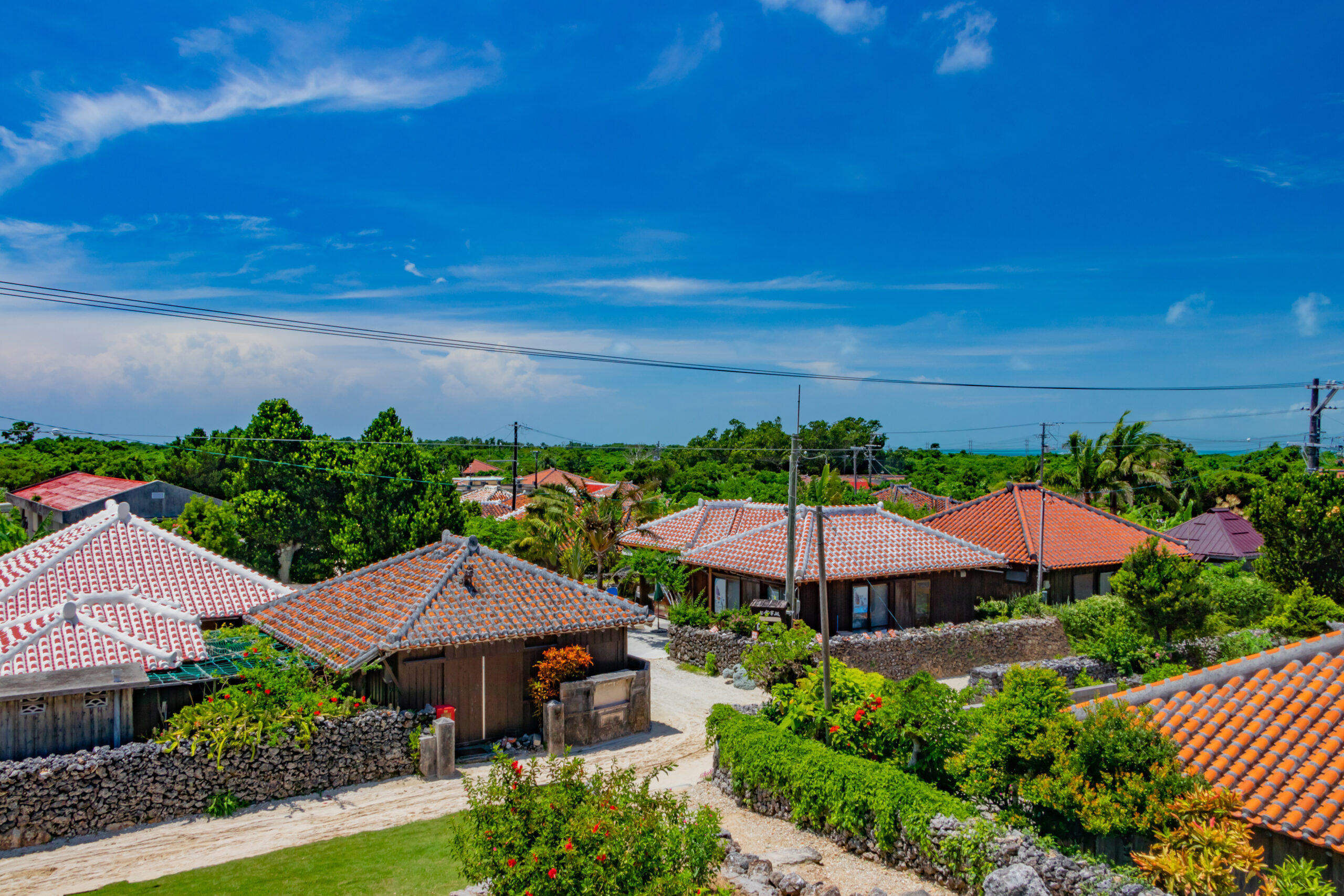 Row of houses with red-tiled roofs and green gardens under a bright blue sky.