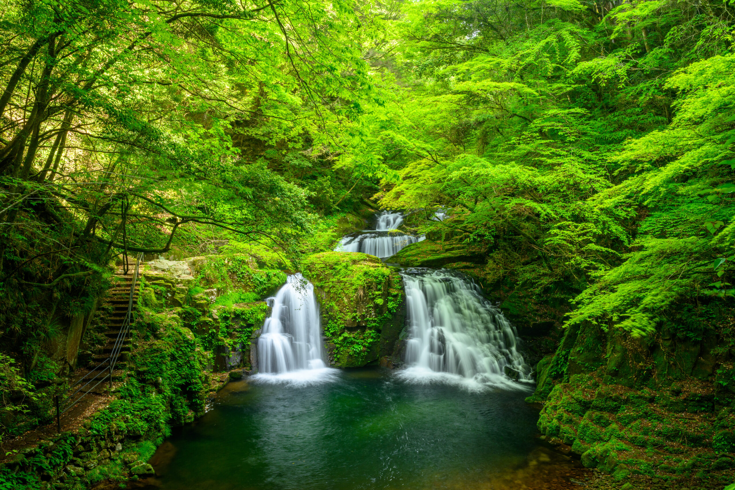 Waterfall cascading over mossy rocks in a lush green forest with a calm pool below