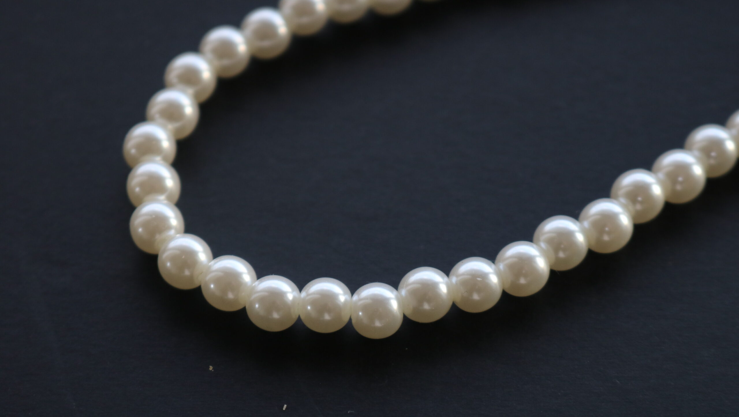 Close-up of a string of white pearls arranged in a curved line on a dark surface.