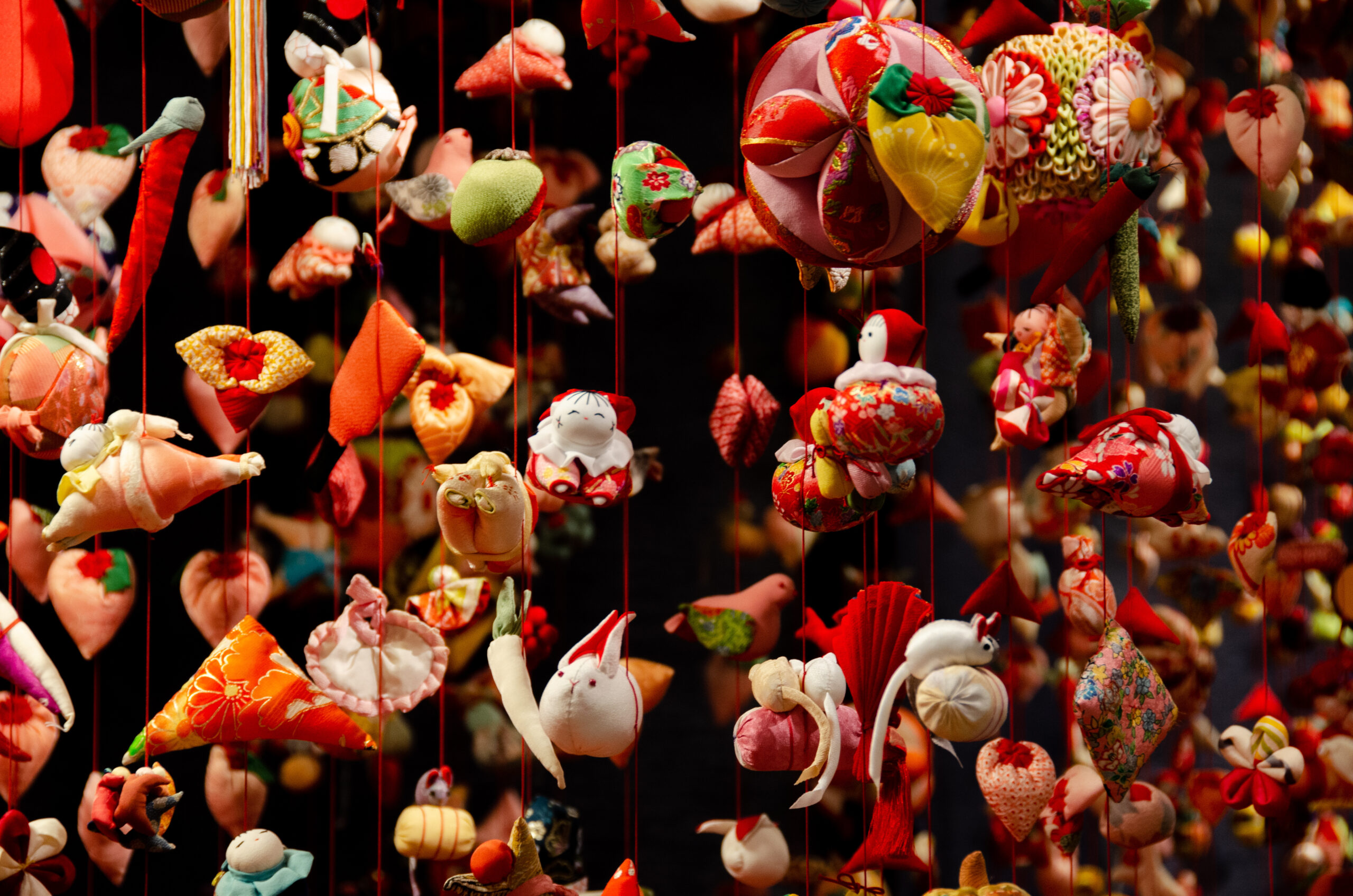 Colorful fabric ornaments hanging on red threads, forming a dense decorative mobile.