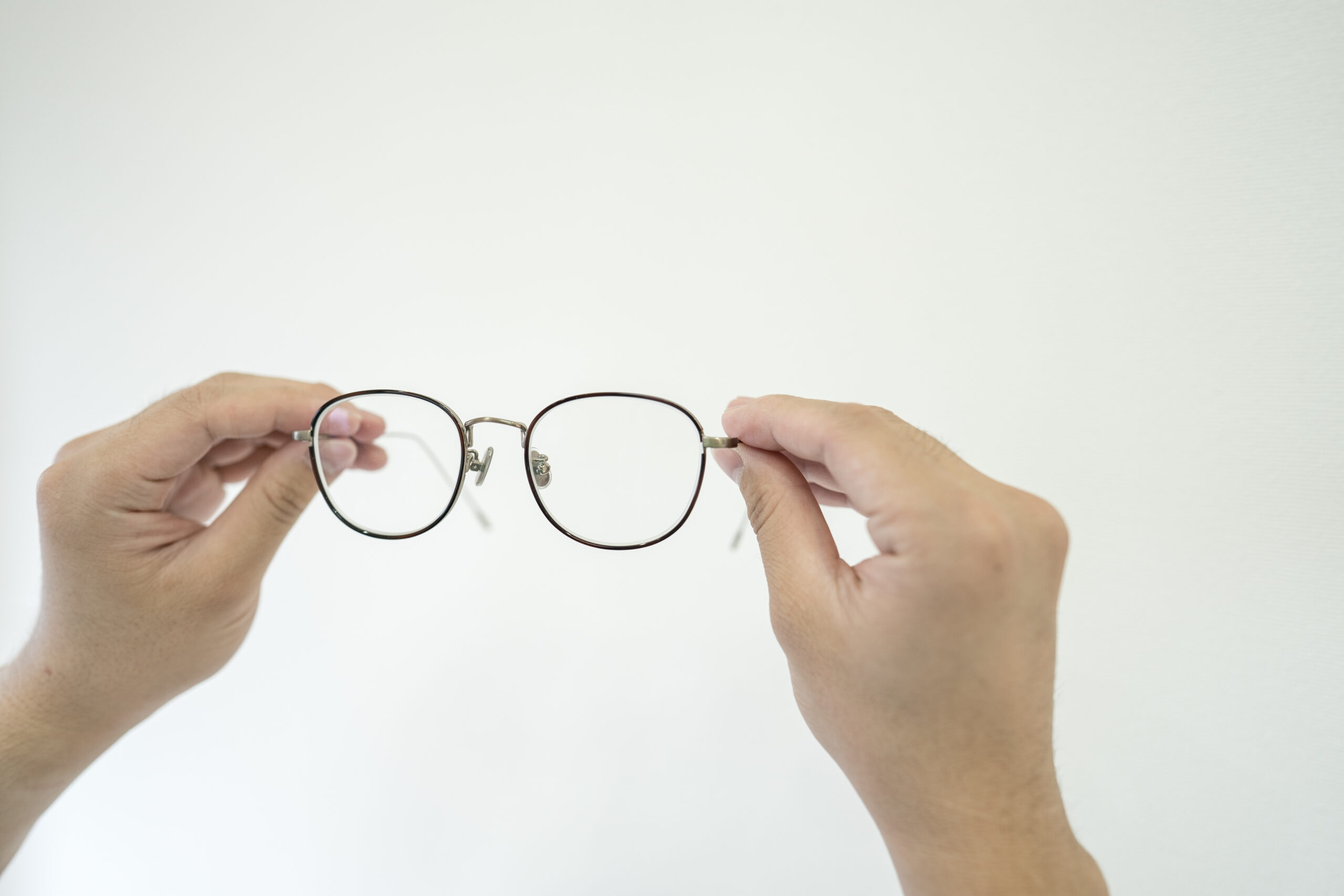 Hands holding round metal eyeglasses against a plain white background.