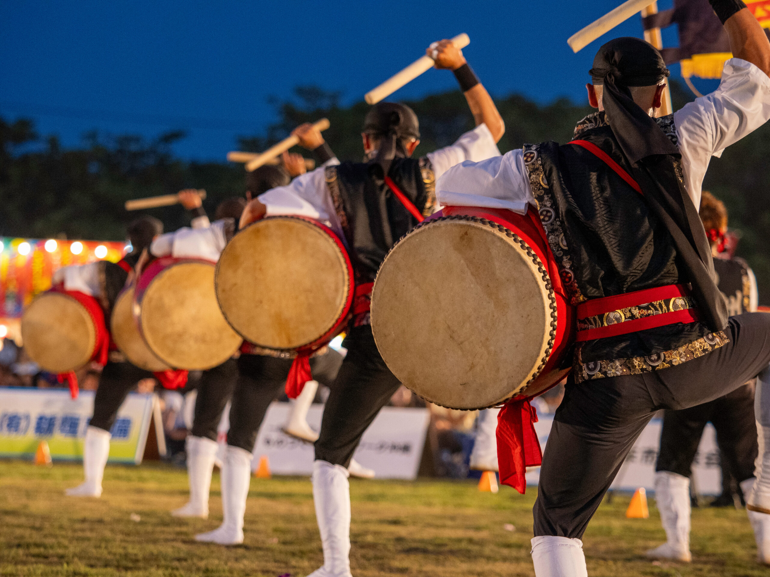Drummers in red-and-black costumes performing at dusk with large circular drums in a parade