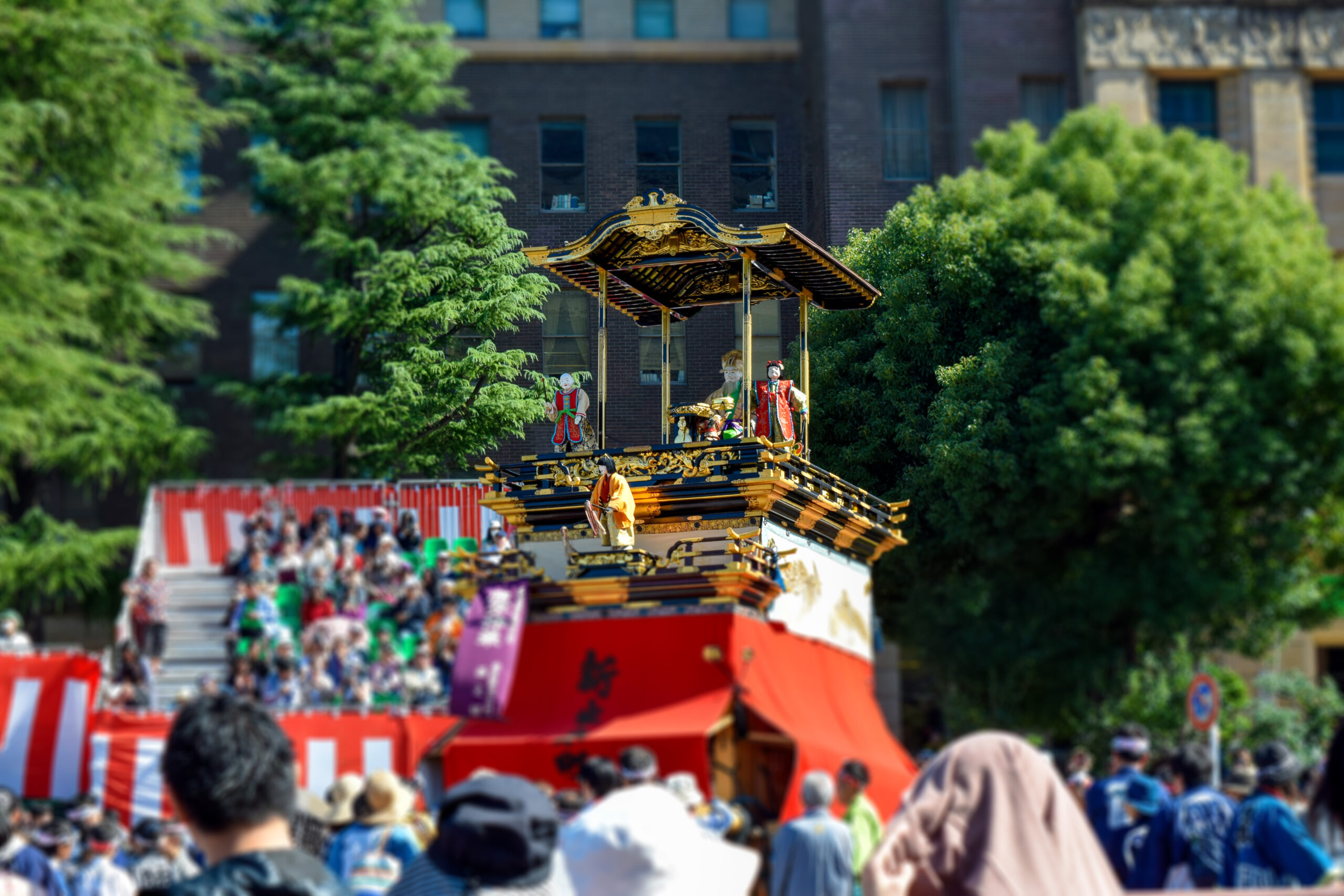Colorful traditional festival float with gold detailing moving through a crowded city street with spectators watching the parade.