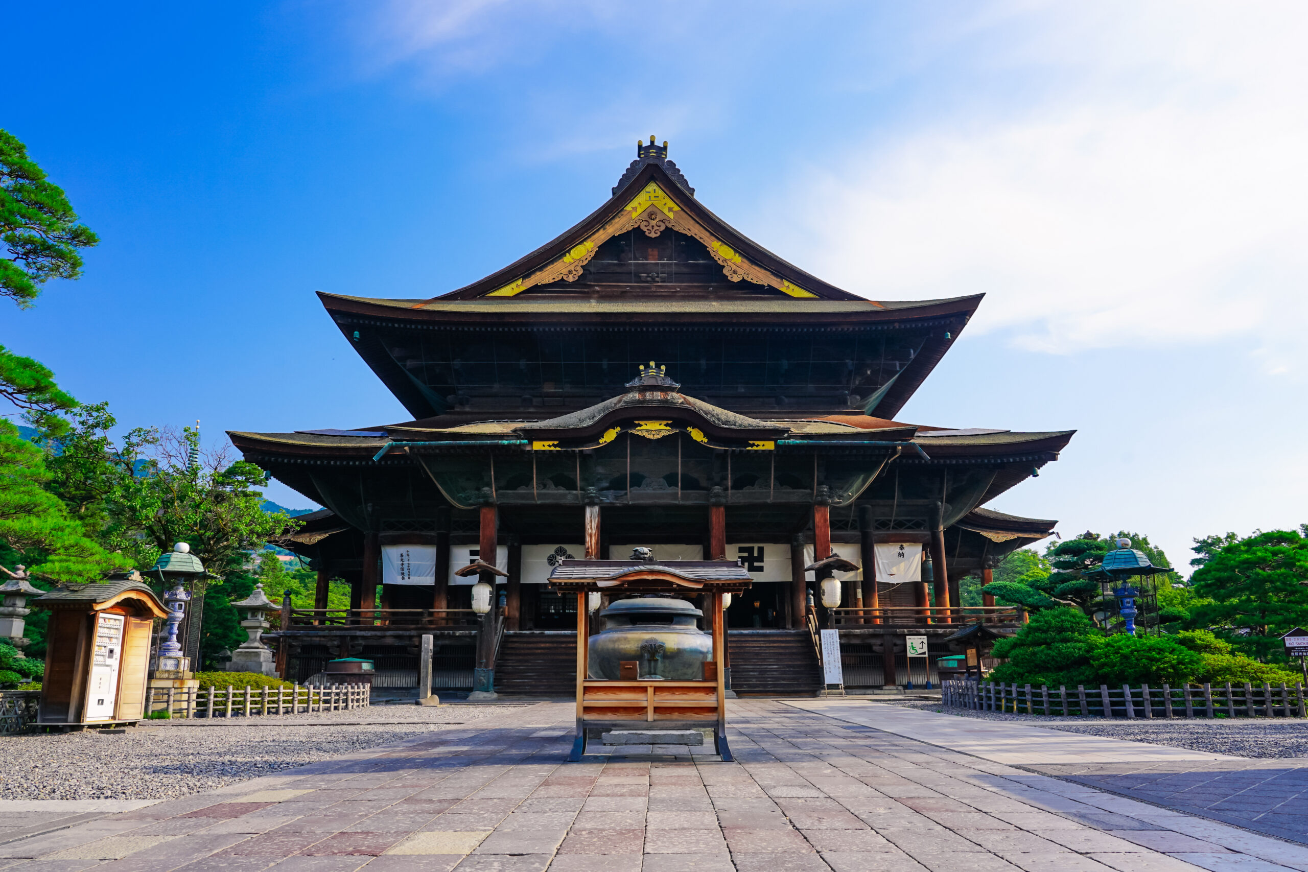 Traditional Japanese temple with multi-tiered, curved roofs in a stone-paved courtyard and surrounding greenery. (informative)