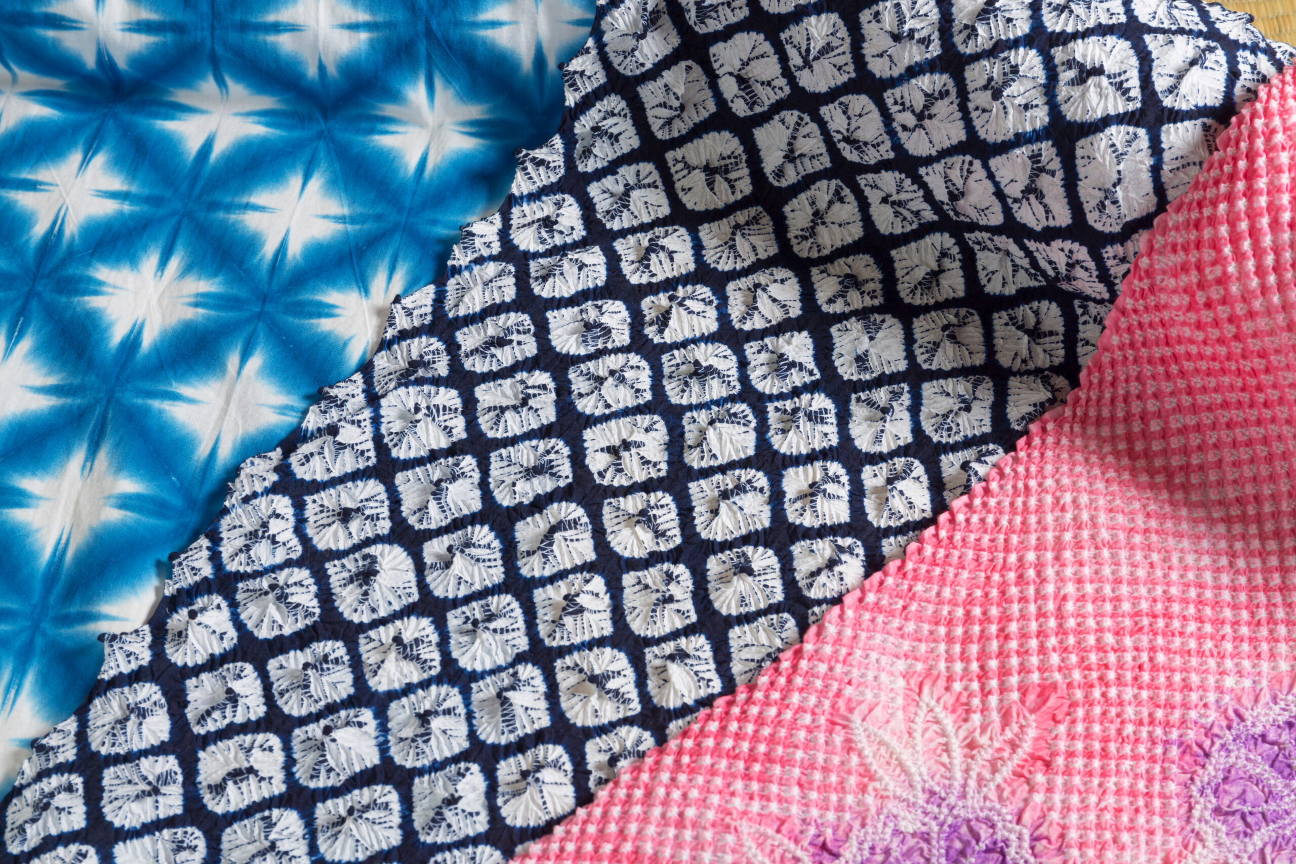Close-up of a quilt showing blue tie-dye, navy with white square patterns, and pink textured fabric pieces.