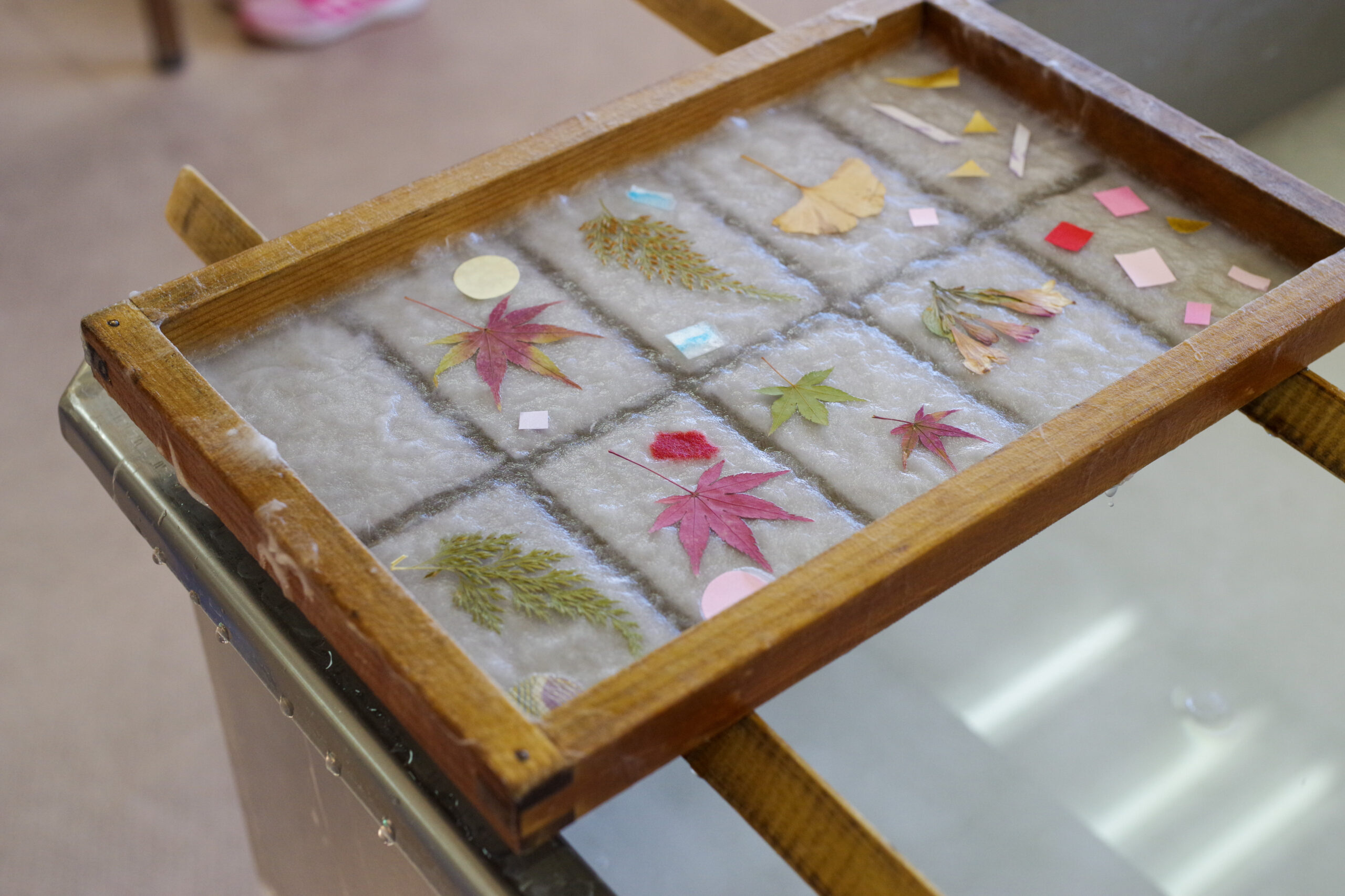Wooden ice tray filled with ice, dried autumn leaves, and small pastel paper squares scattered on top (decorative display).