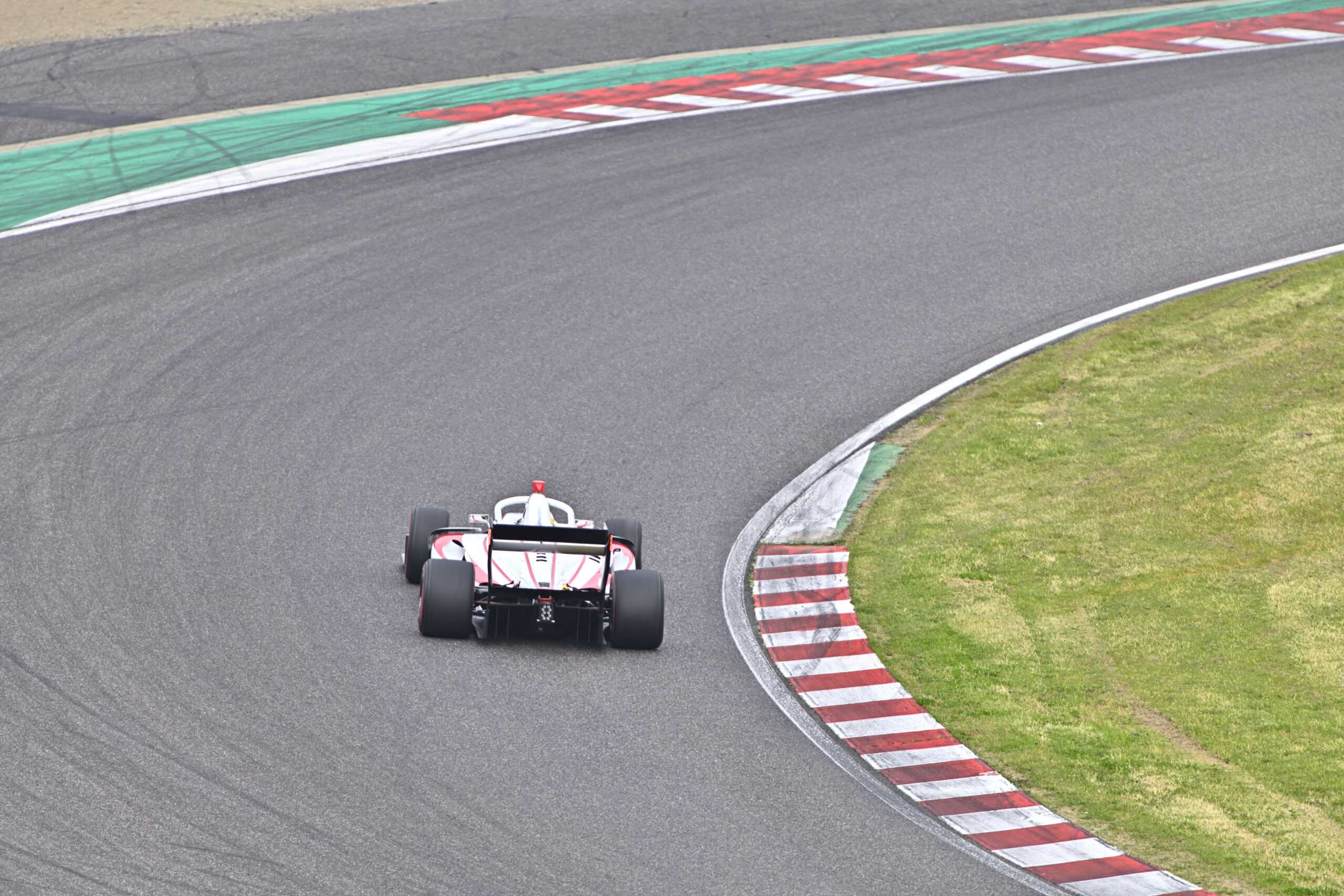Race car navigating a sharp curve on a race track, red-and-white car near red-and-white curb and green run-off area