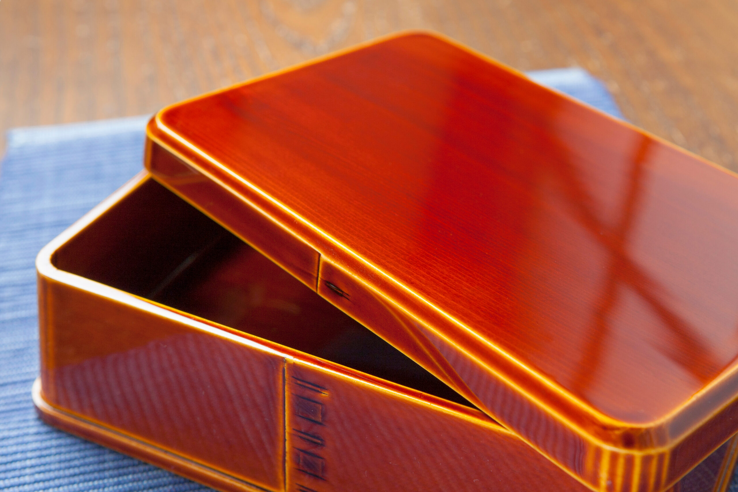 Close-up of glossy orange wooden boxes stacked on a blue fabric surface with curved edges visible.