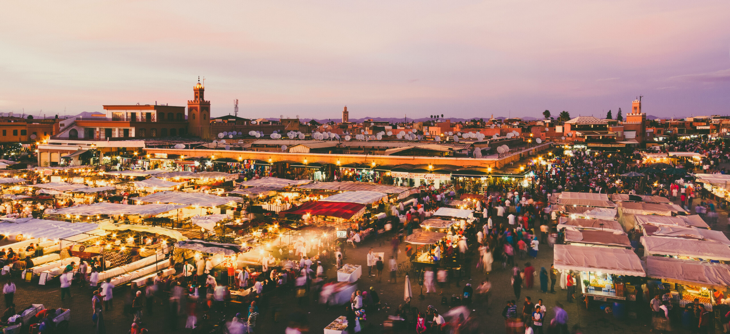 Bustling outdoor market at dusk with rows of illuminated stalls and crowds