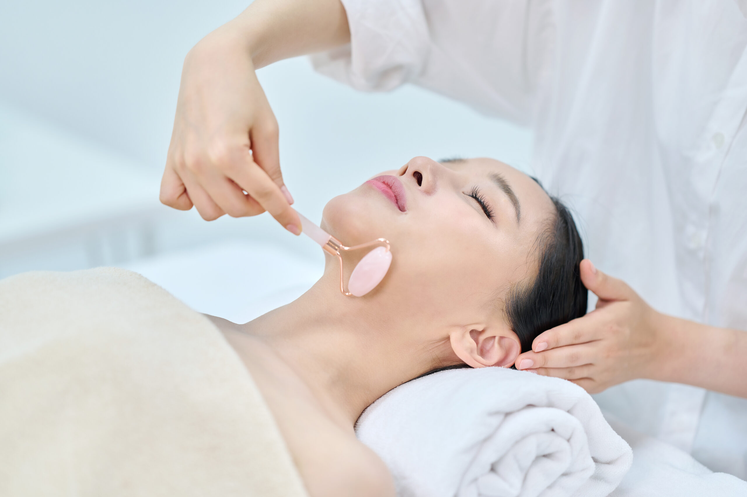Woman lying with eyes closed while a therapist uses a handheld facial tool on her face in a spa setting.