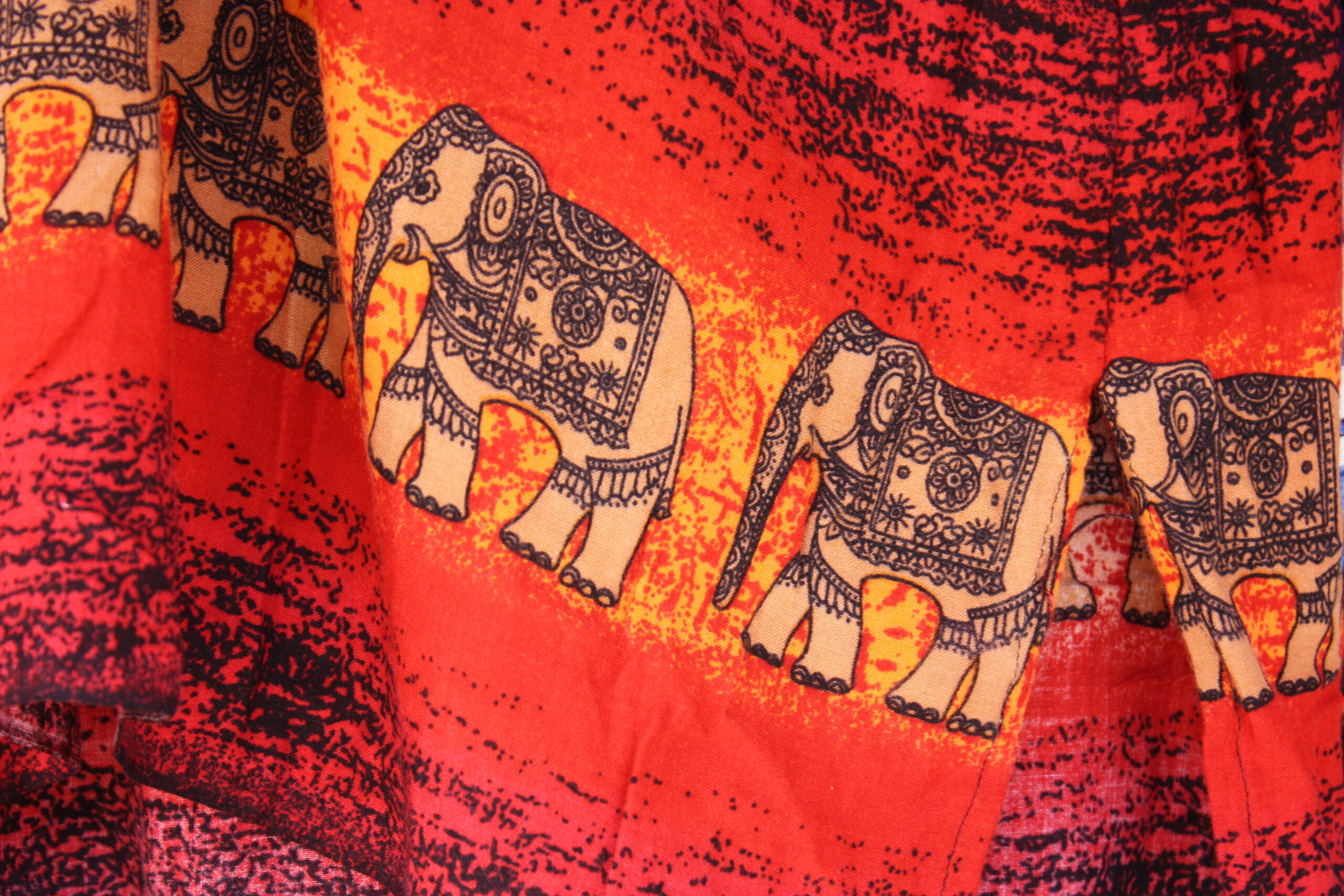 Bright red fabric with repeating white elephants outlined in blue and lace-like details around each elephant.