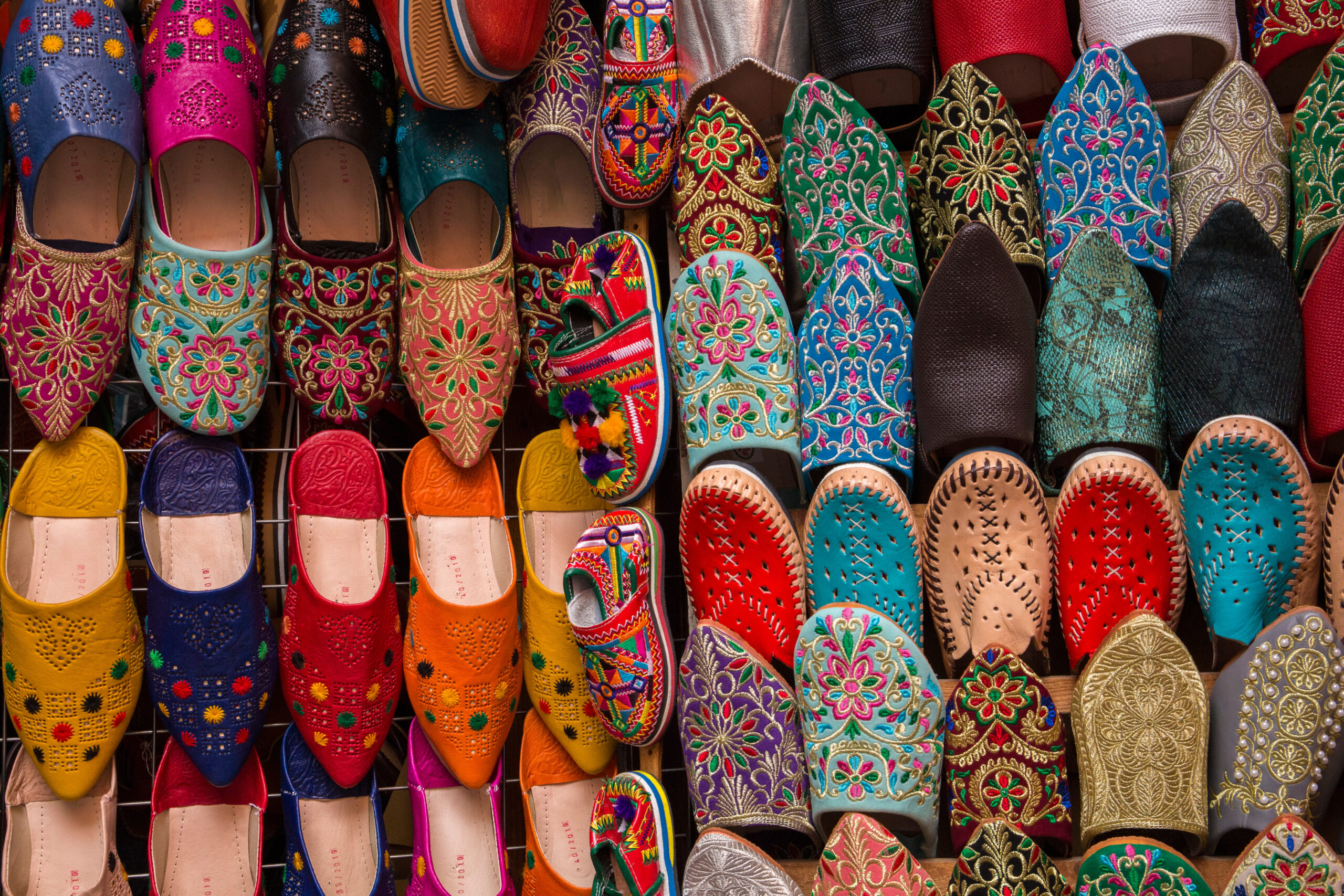 Row of bright embroidered flat shoes with floral patterns on a display rack, showcasing reds, blues, greens, and yellows.