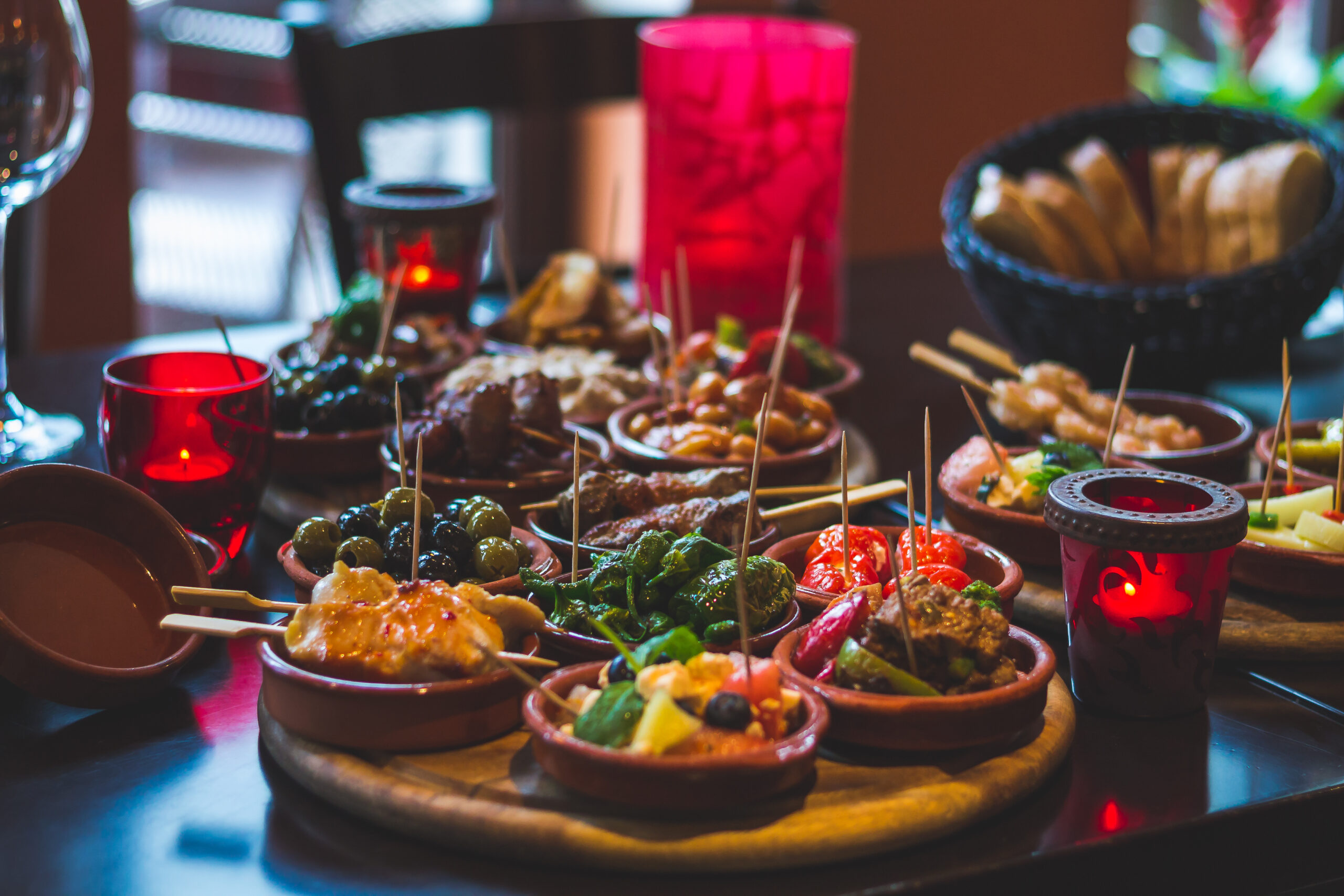 Assorted tapas on wooden boards with olives, skewers, vegetables, and bread at a candlelit table.