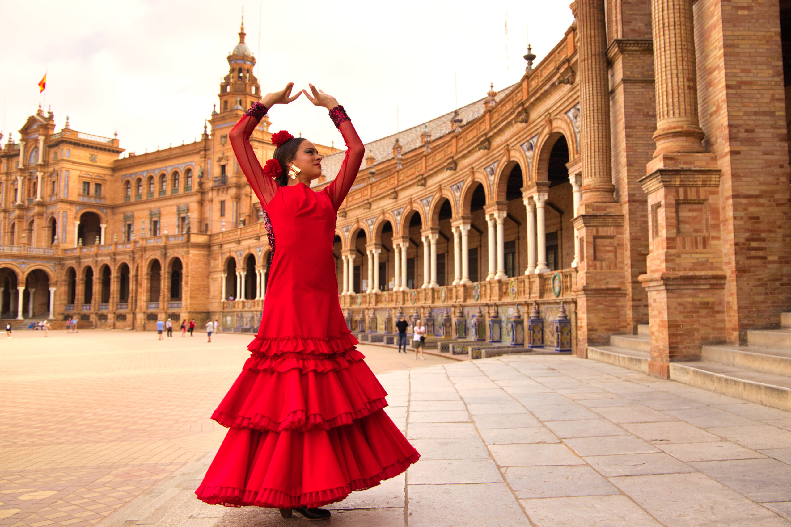 Flamenco dancer in a bright red dress performing in front of Seville’s Plaza de España arches and brick columns.