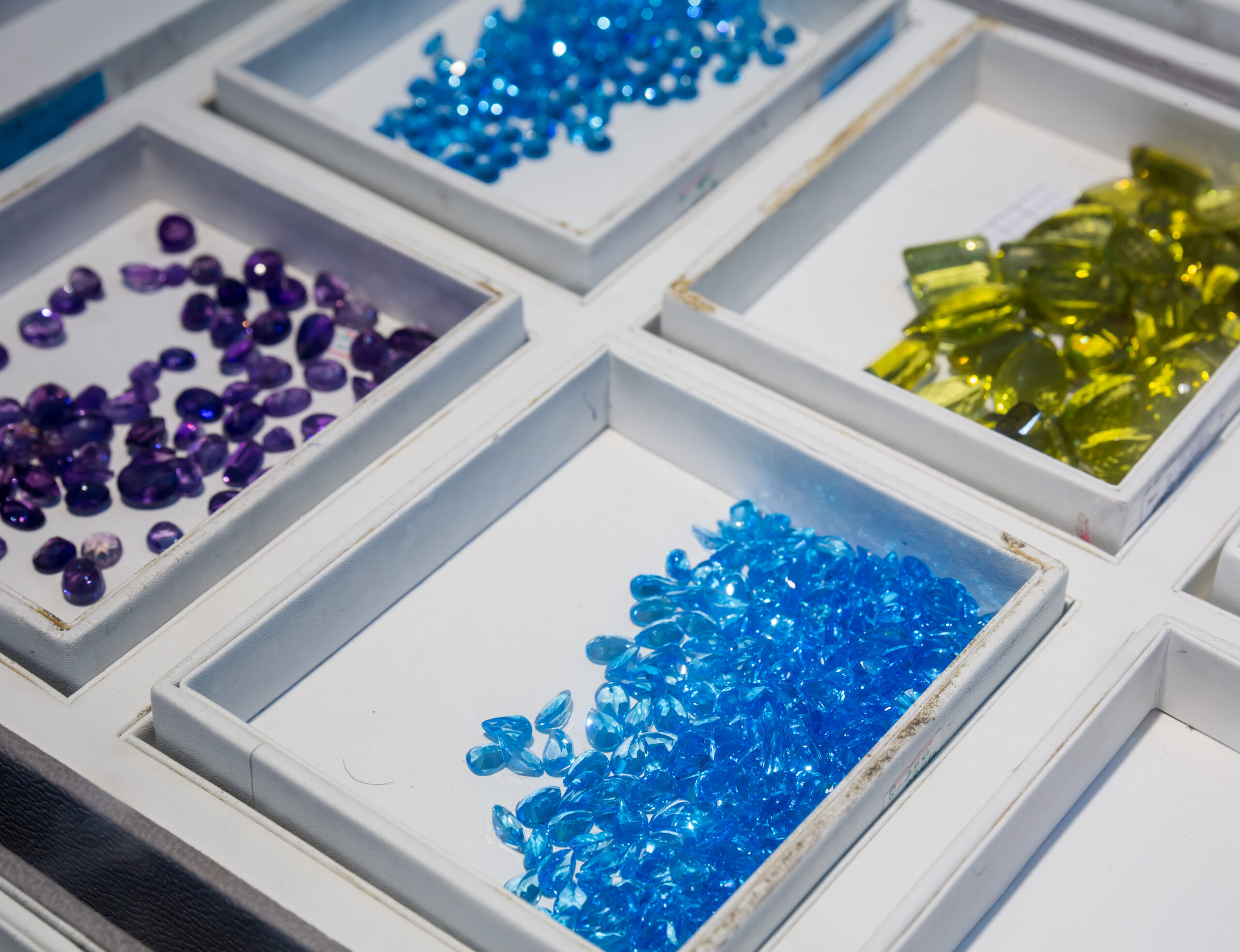 Assorted colorful beads in white display trays: purple, blue, and yellow pieces organized by color.