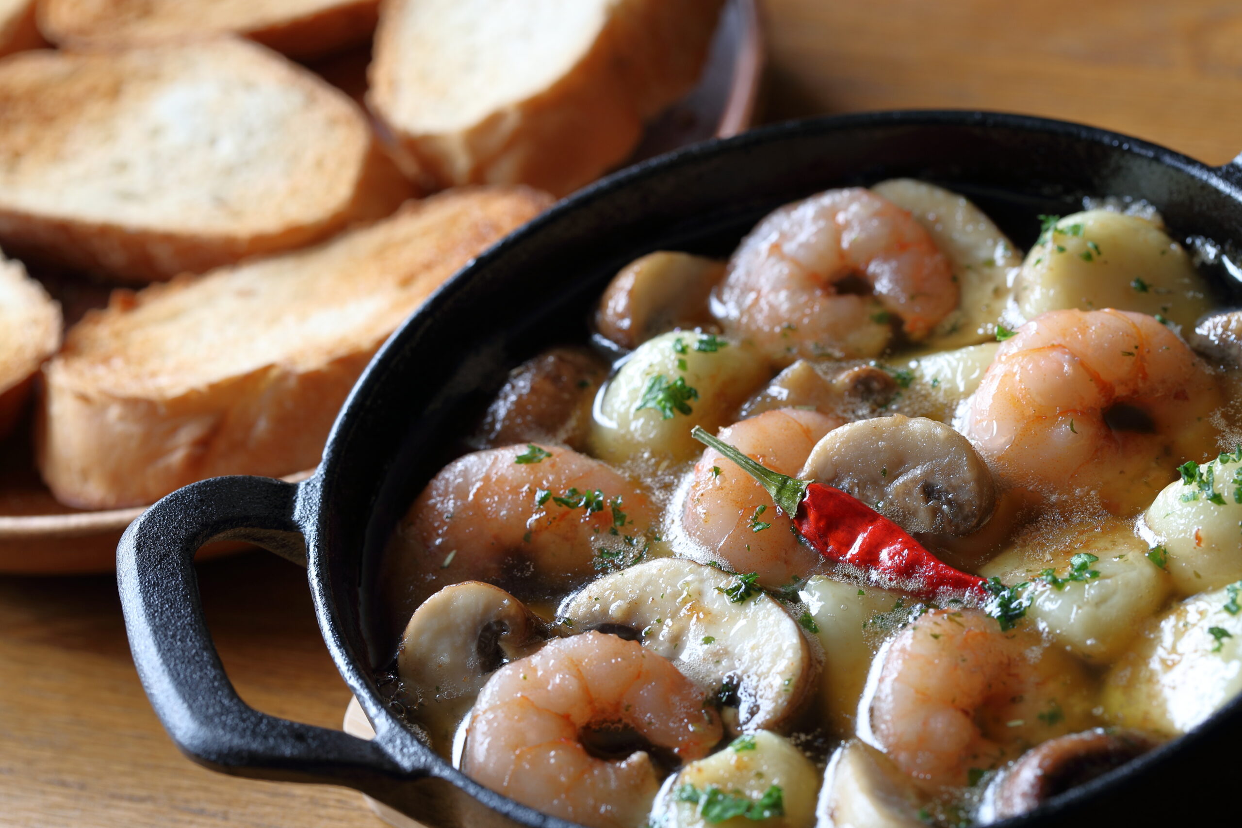 Shrimp and potatoes in a creamy herb sauce in a cast-iron skillet, with toasted bread in the background