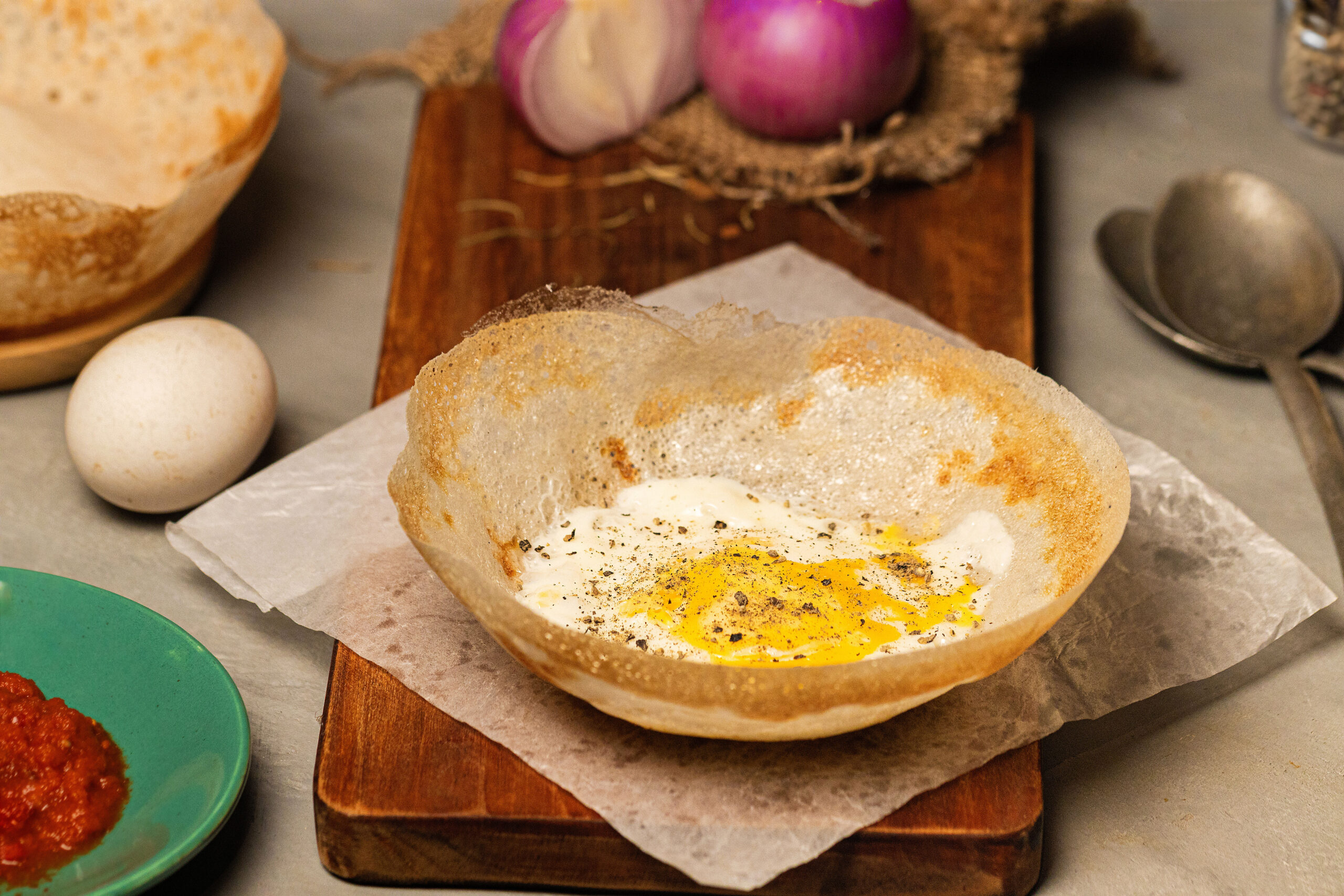 Open-faced fried egg in a toasted bagel half, sprinkled with pepper, resting on parchment on a wooden board.