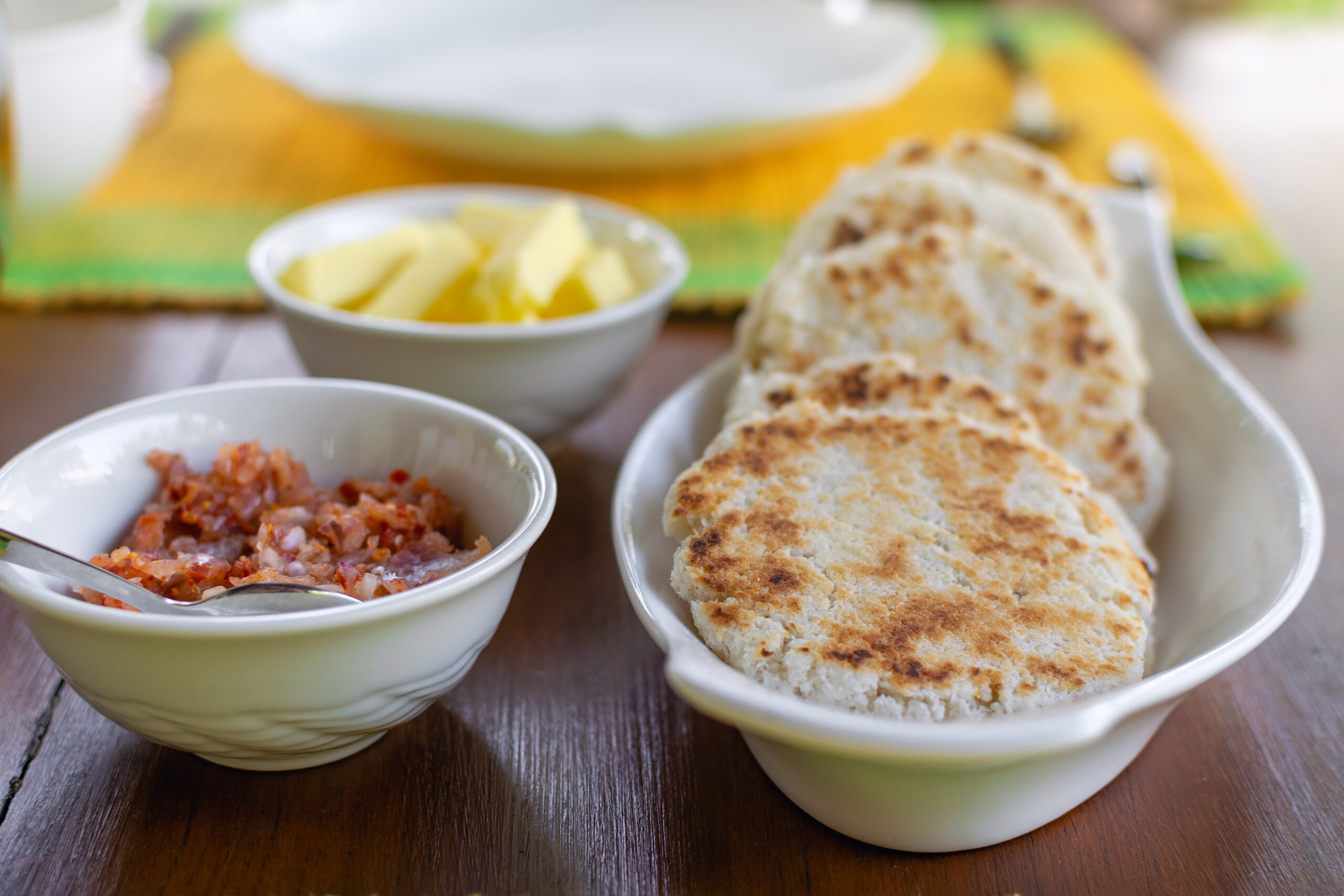 Toasted bread slices on a white plate with bowls of butter and jam on a wooden table in the background.