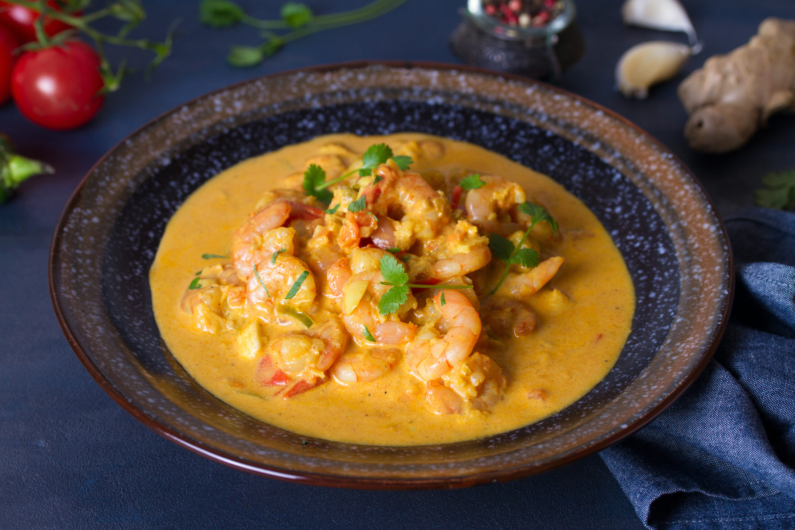 Creamy orange shrimp curry with shrimp chunks and cilantro garnish in a dark bowl on a blue surface.