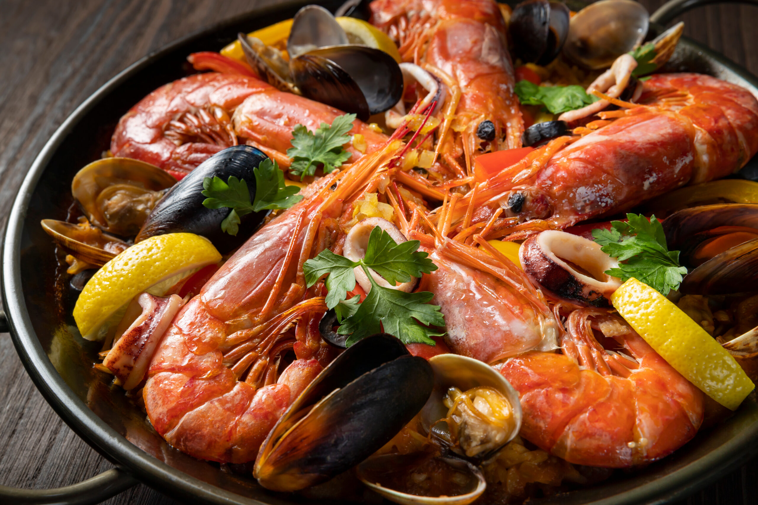 Seafood paella in a skillet with shrimp, mussels, clams, lemon wedges and parsley.